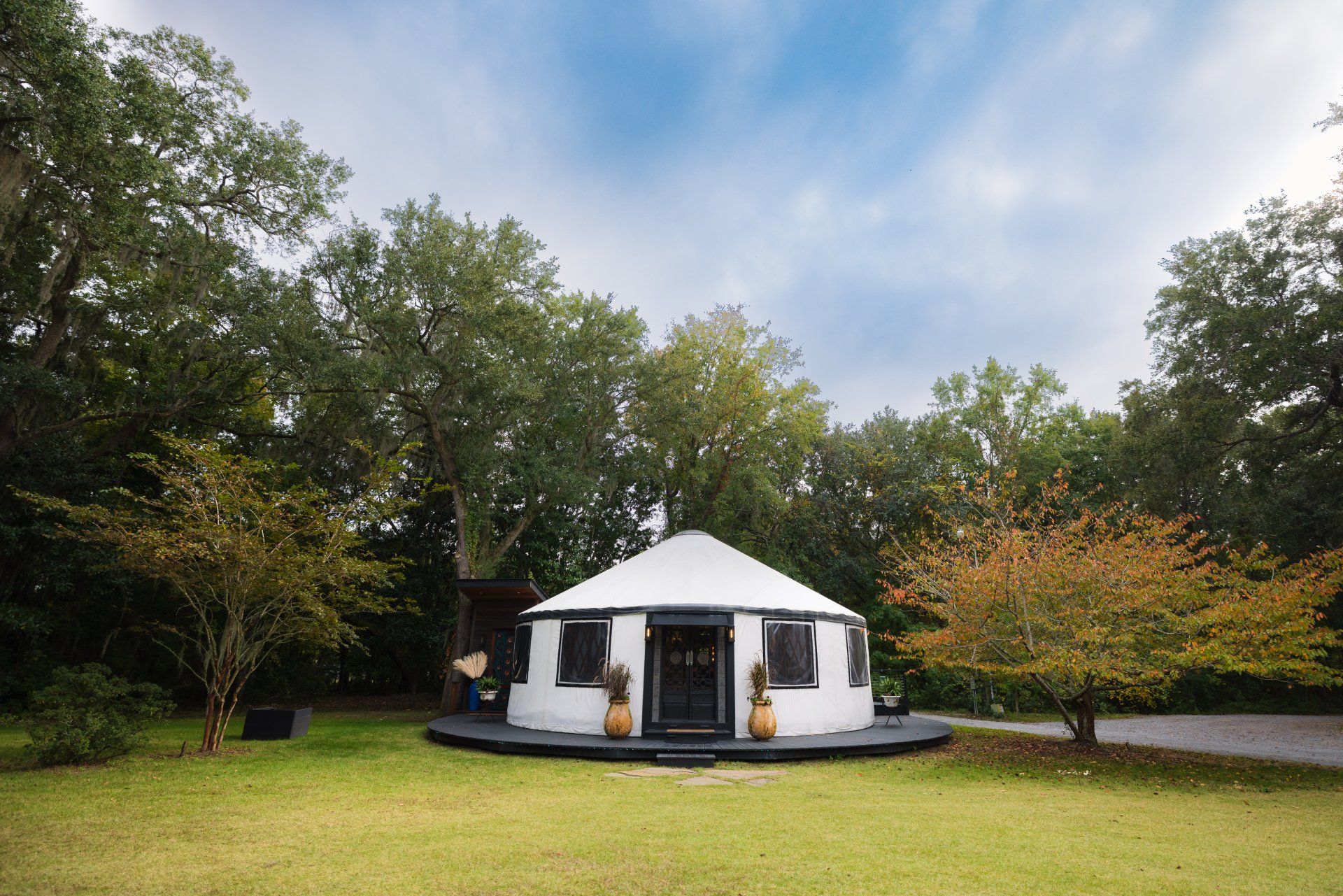 White tent pavilion in a grassy park surrounded by trees under a cloudy sky