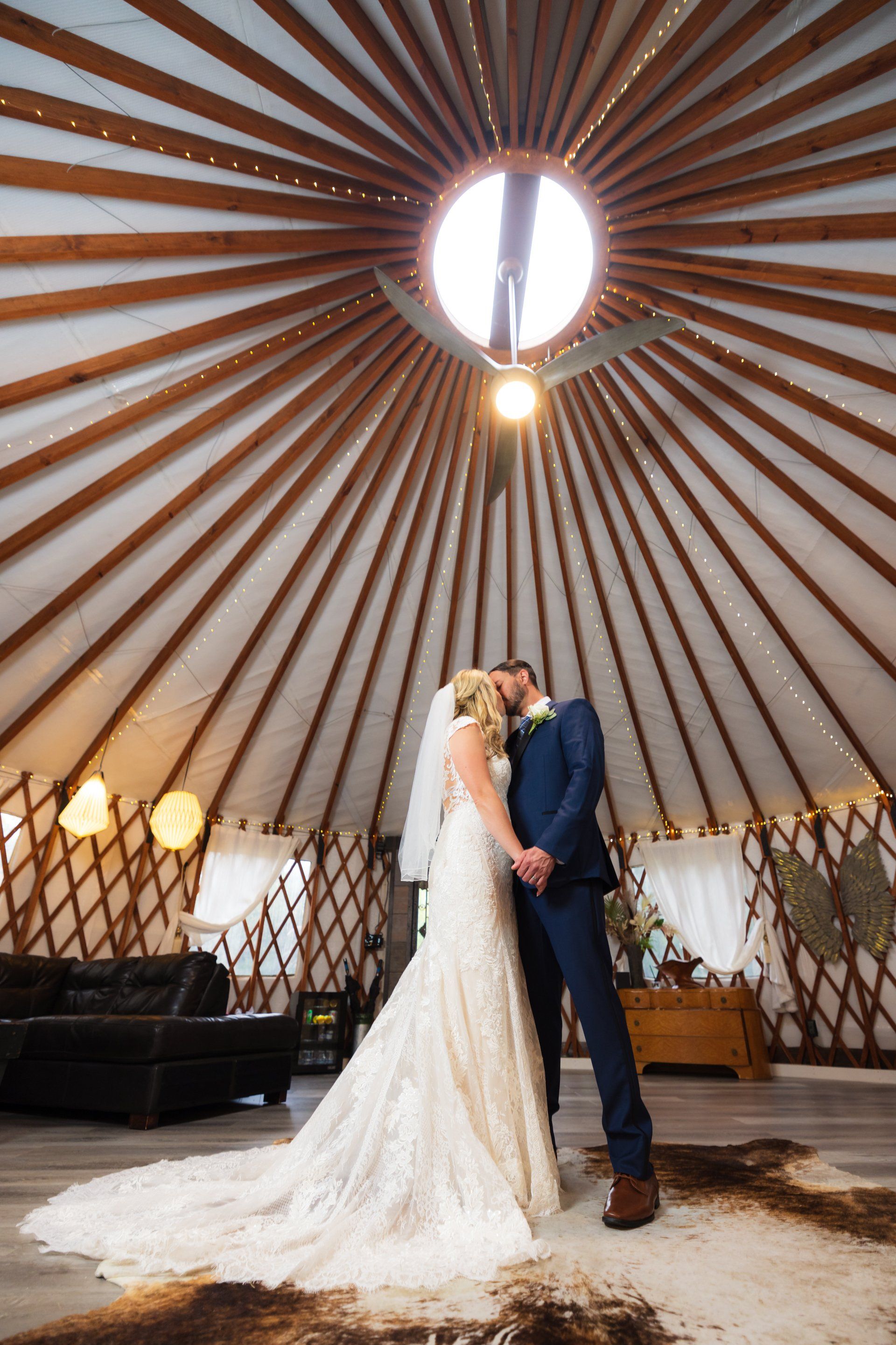 Bride and groom kiss beneath a circular skylight in a teepee-style wedding tent.