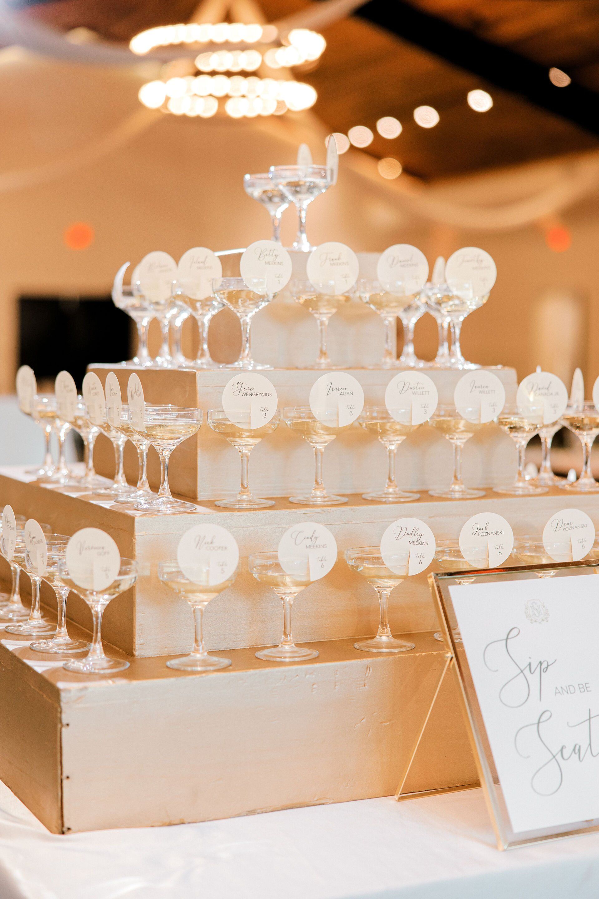 Tiered champagne tower of clear glasses on a gold table at a warmly lit event venue