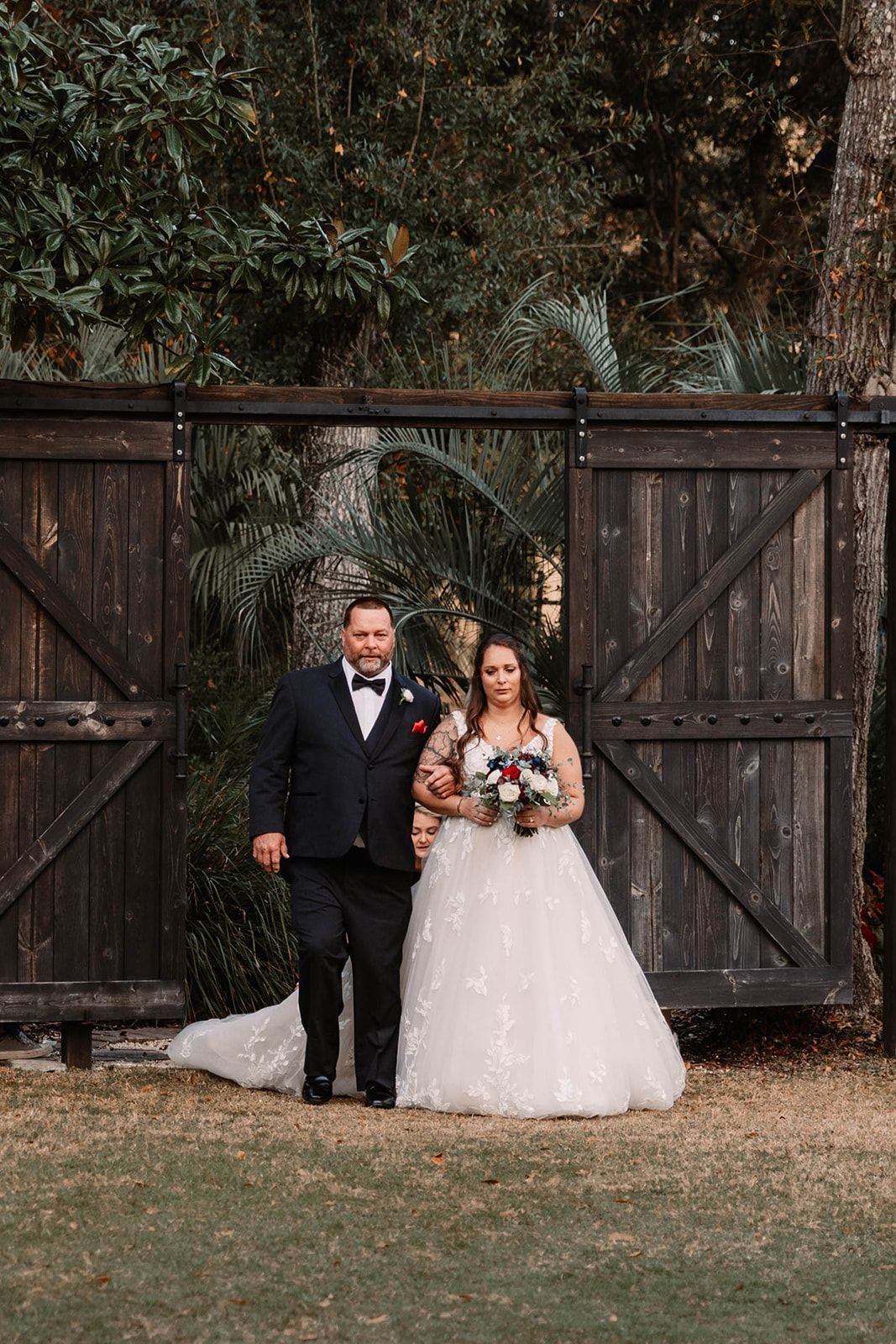 Bride and groom standing in front of rustic wooden doors outdoors, holding hands and smiling