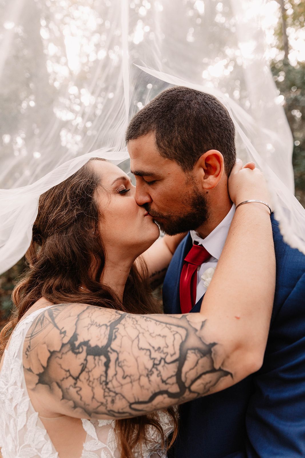 Couple kissing under a sheer canopy, bride in white and groom in a navy suit, outdoors