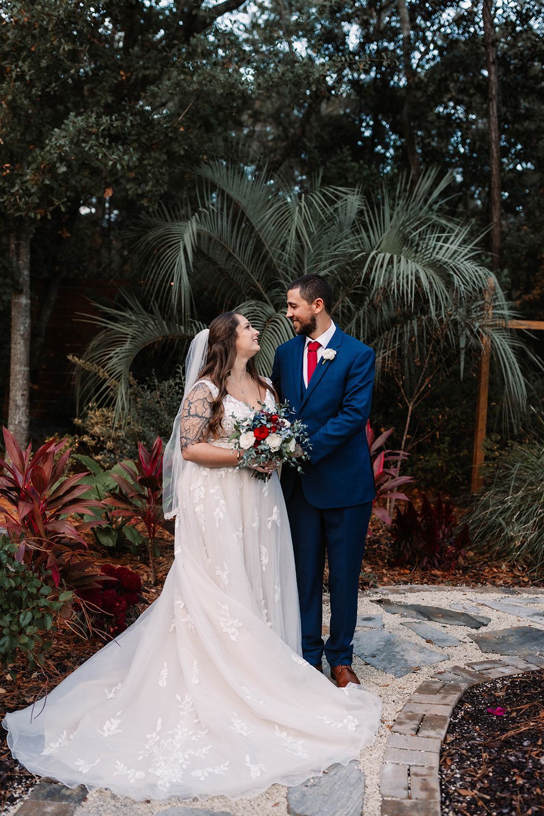 Bride and groom in a garden, holding hands and smiling on a stone path.