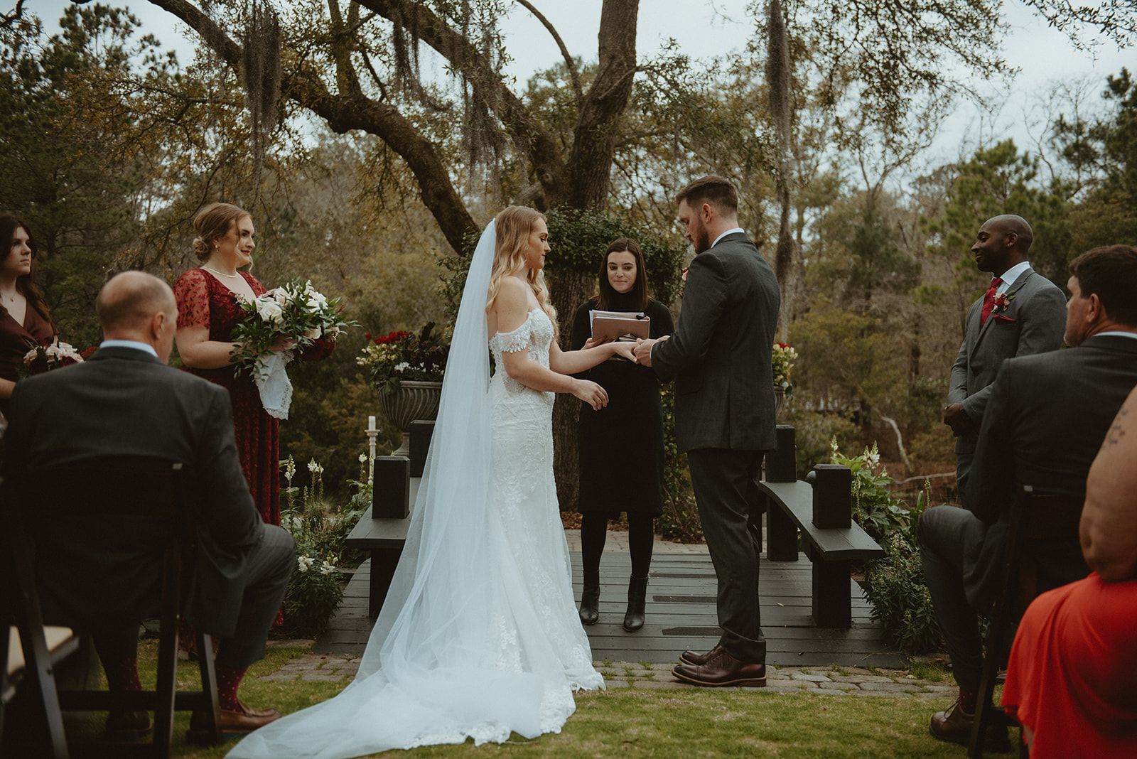 Outdoor wedding ceremony with couple exchanging rings beside floral arrangements and seated guests