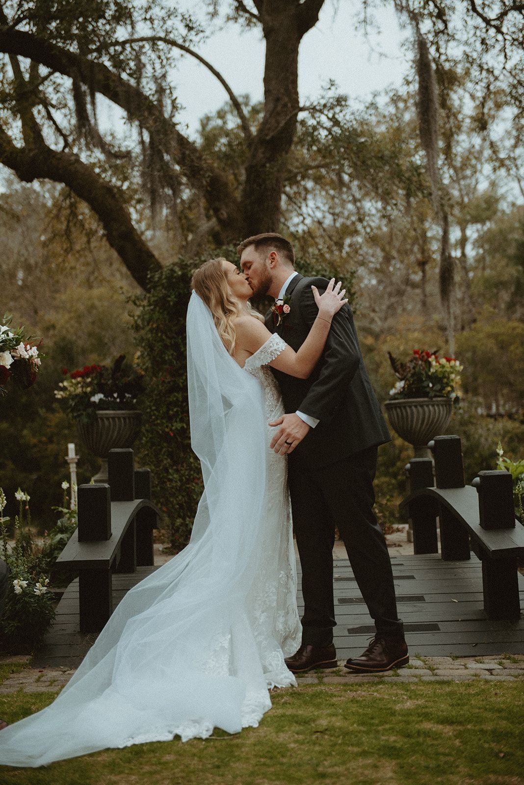 Bride and groom kissing in a garden under a tree, bride in a long veil and train