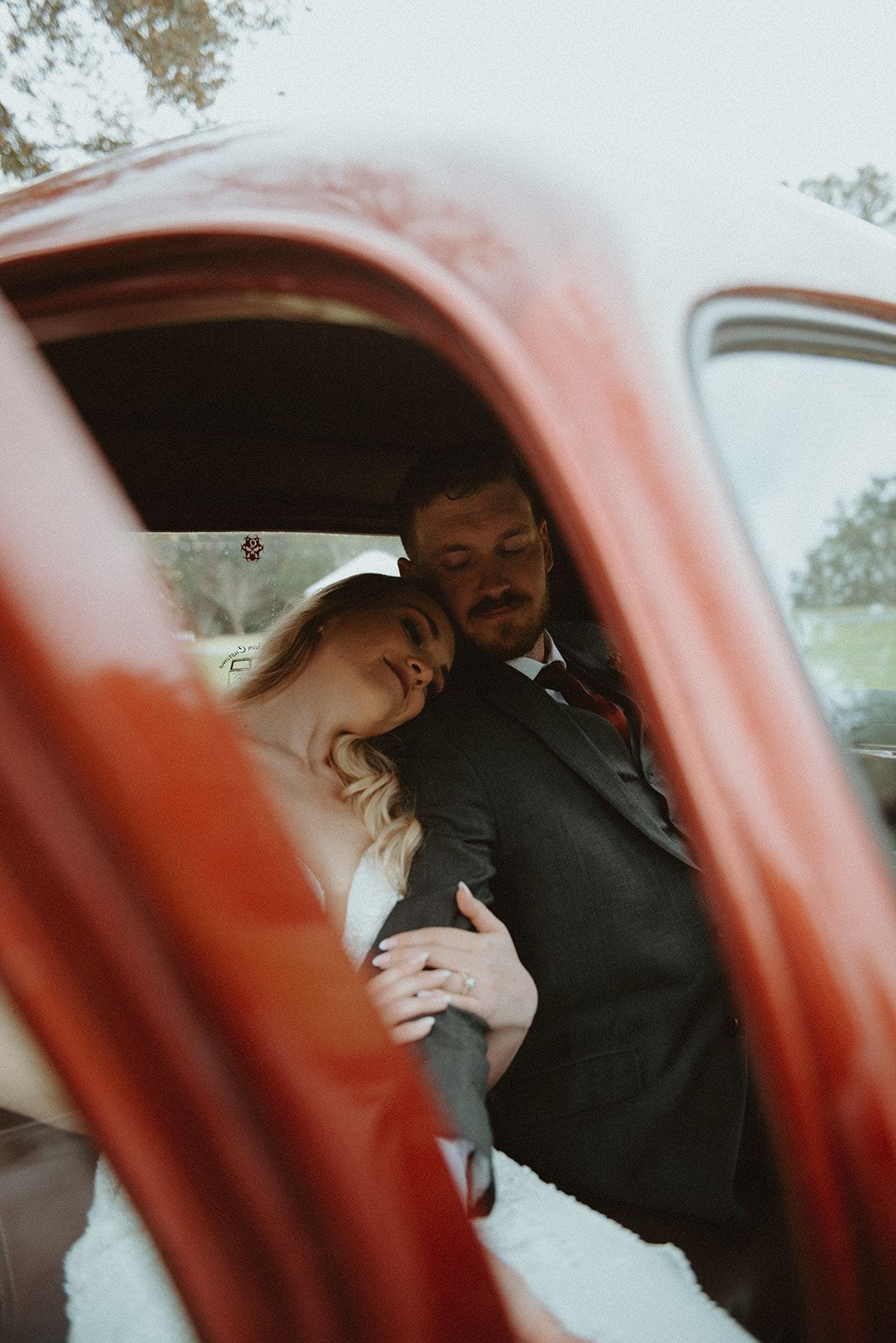 Two people leaning together inside a red vehicle, seen through the open door in a rainy setting