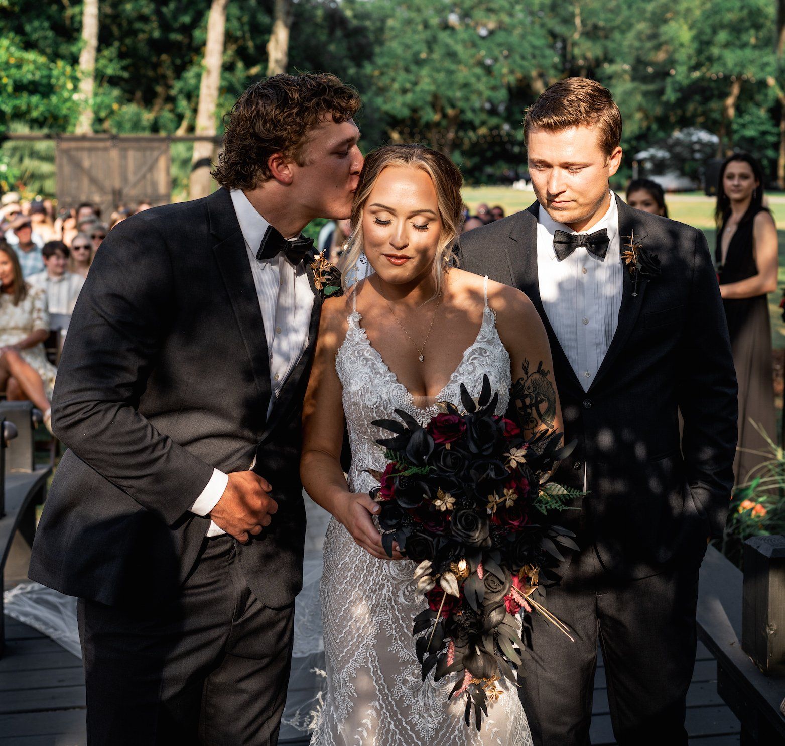 Three wedding guests walking outdoors, with the bride in a white dress holding a bouquet.