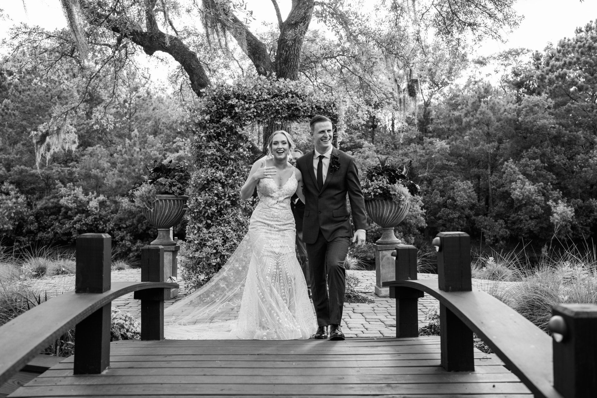 Bride and groom walking on a wooden bridge in a garden, in black and white.