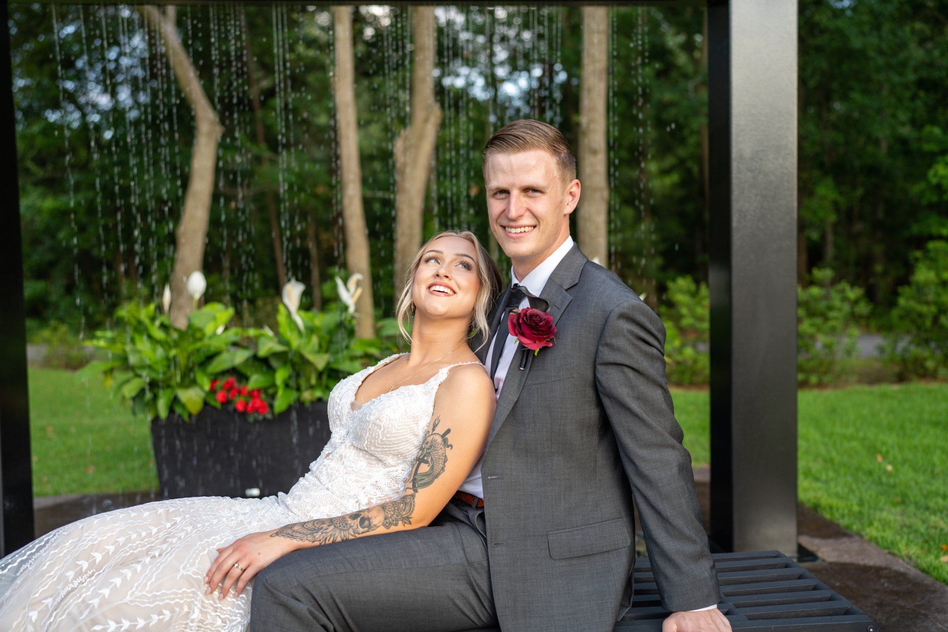 Bride and groom seated on a bench outdoors, smiling in a garden setting.