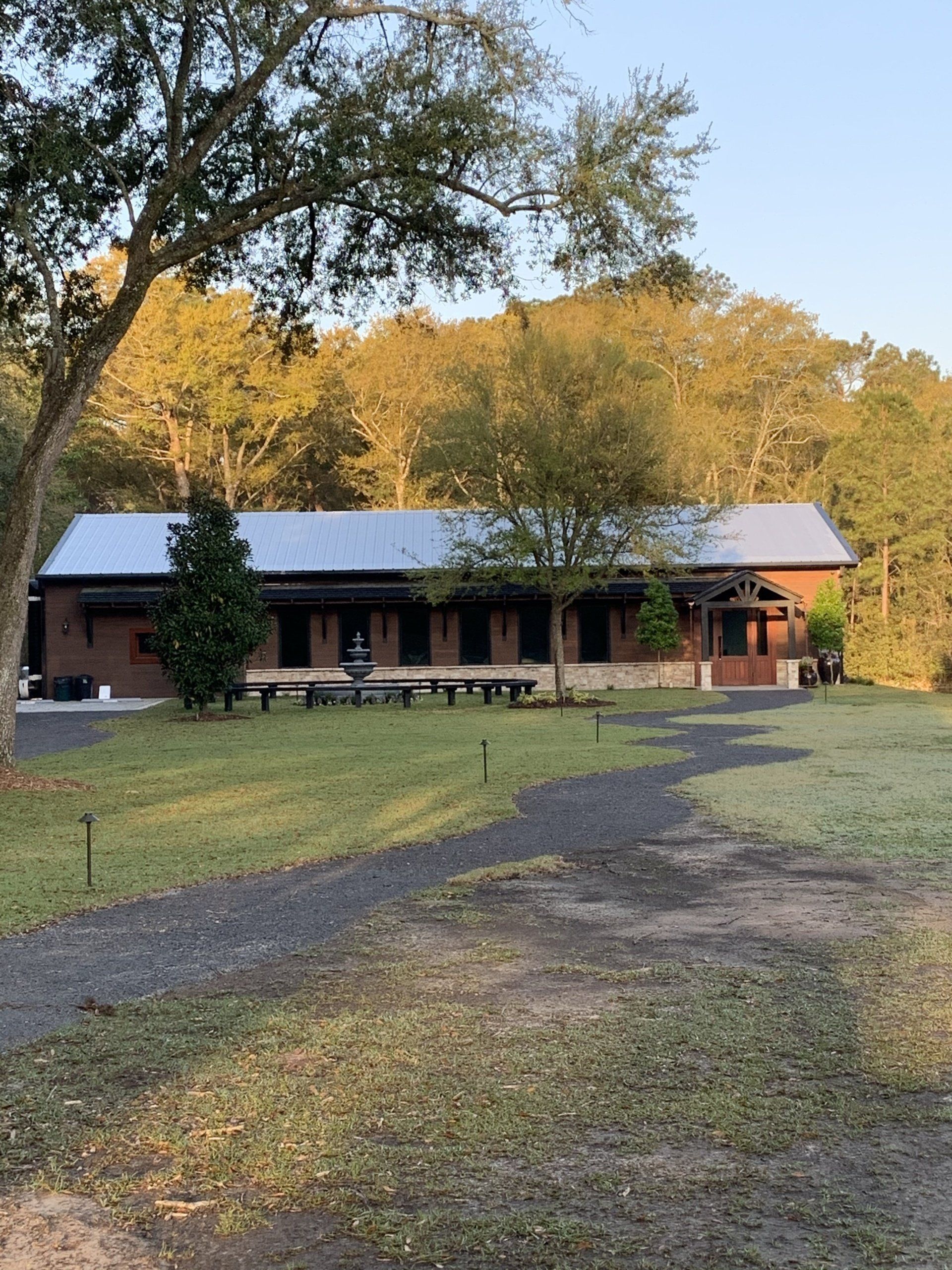 Rural lodge with a metal roof, porch, and gravel drive surrounded by trees at sunset