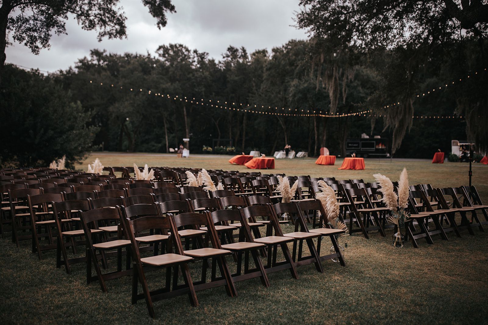 Rows of wooden chairs facing an outdoor stage with red umbrellas in a grassy park