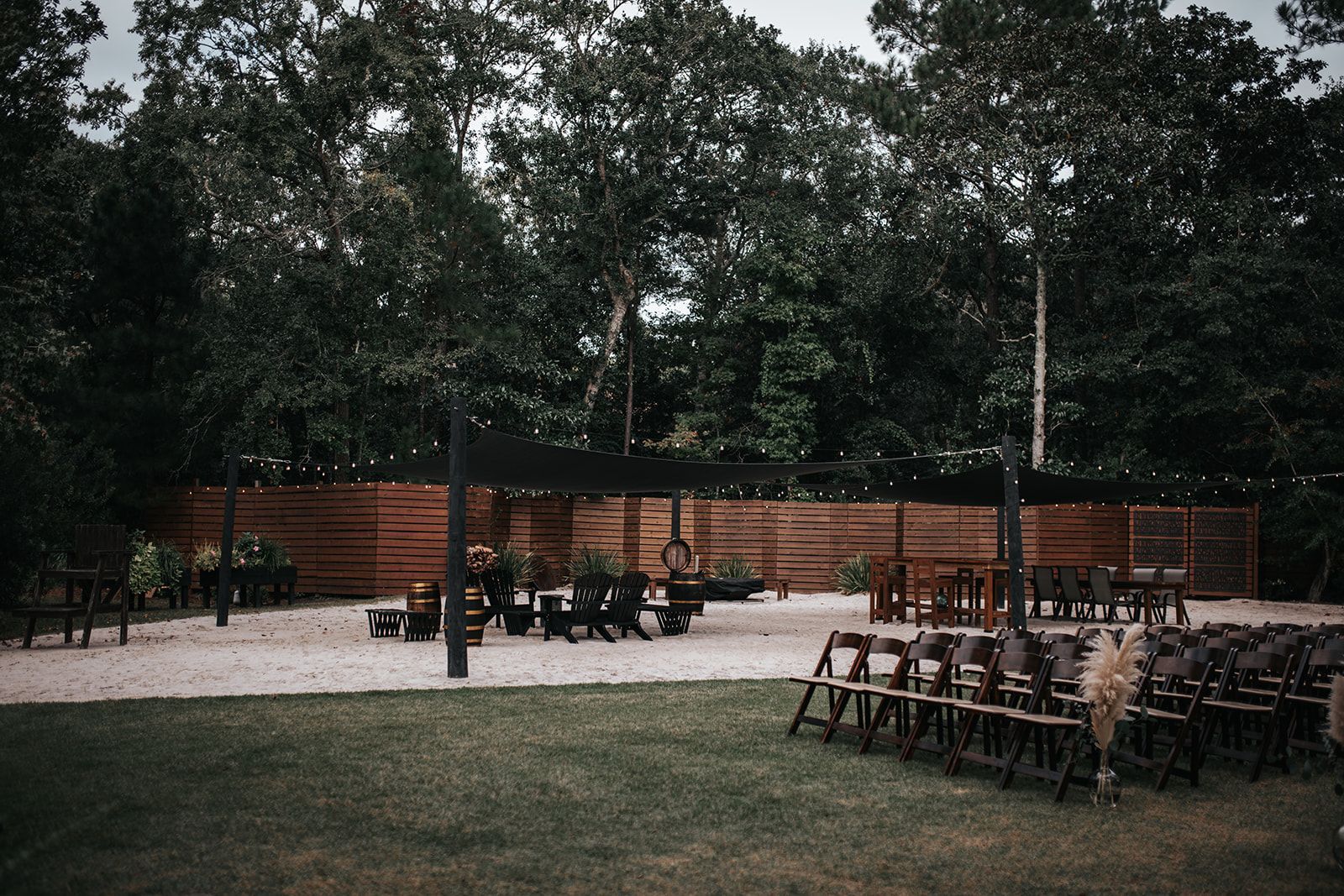 Outdoor patio with wooden fence, string lights, and tables and chairs under trees