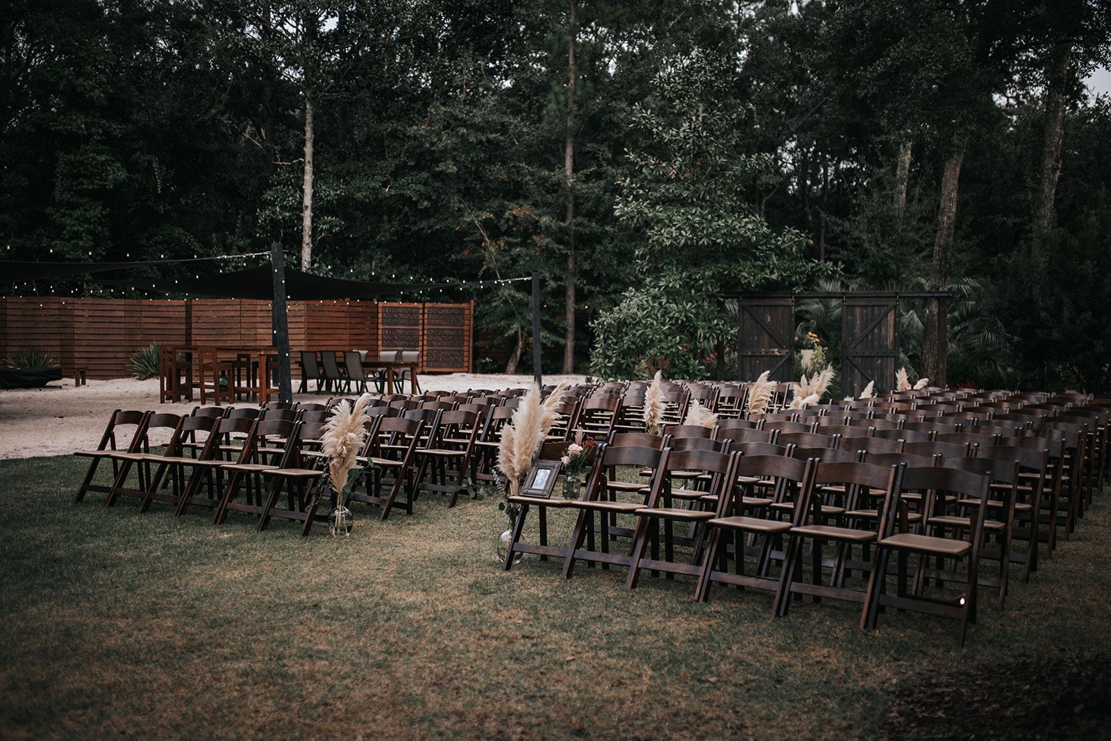 Outdoor wedding reception with rows of chairs and a wooden decked stage in a wooded clearing