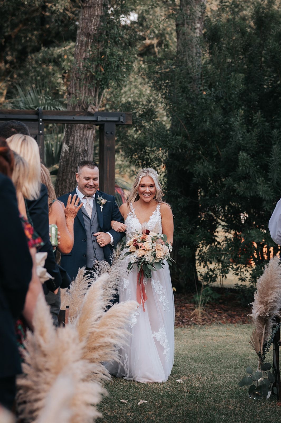 Bride and groom walking down an outdoor aisle, smiling, with guests lining the path.