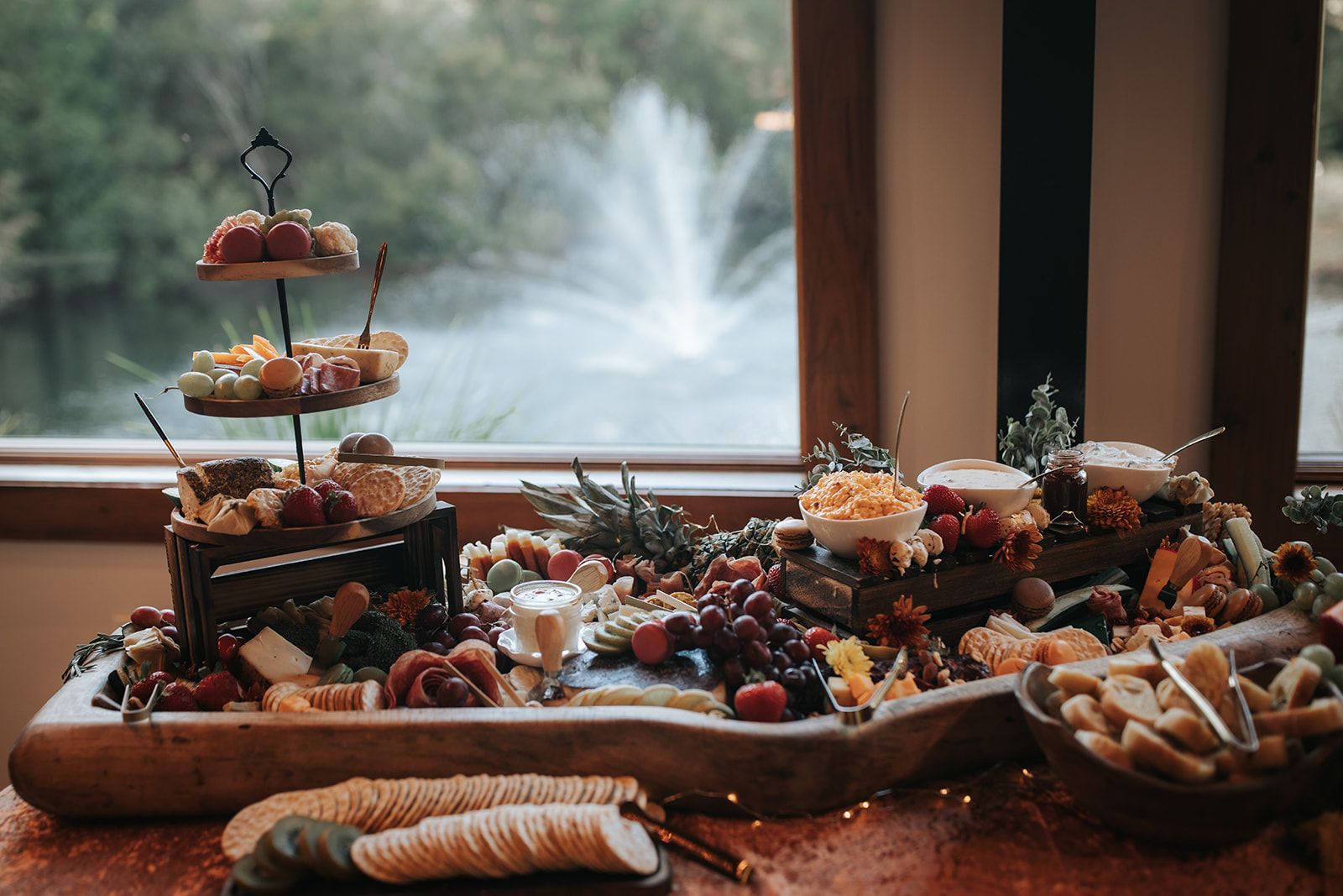 Dessert buffet on a table by a window, with pastries, fruit, and a fountain in the background