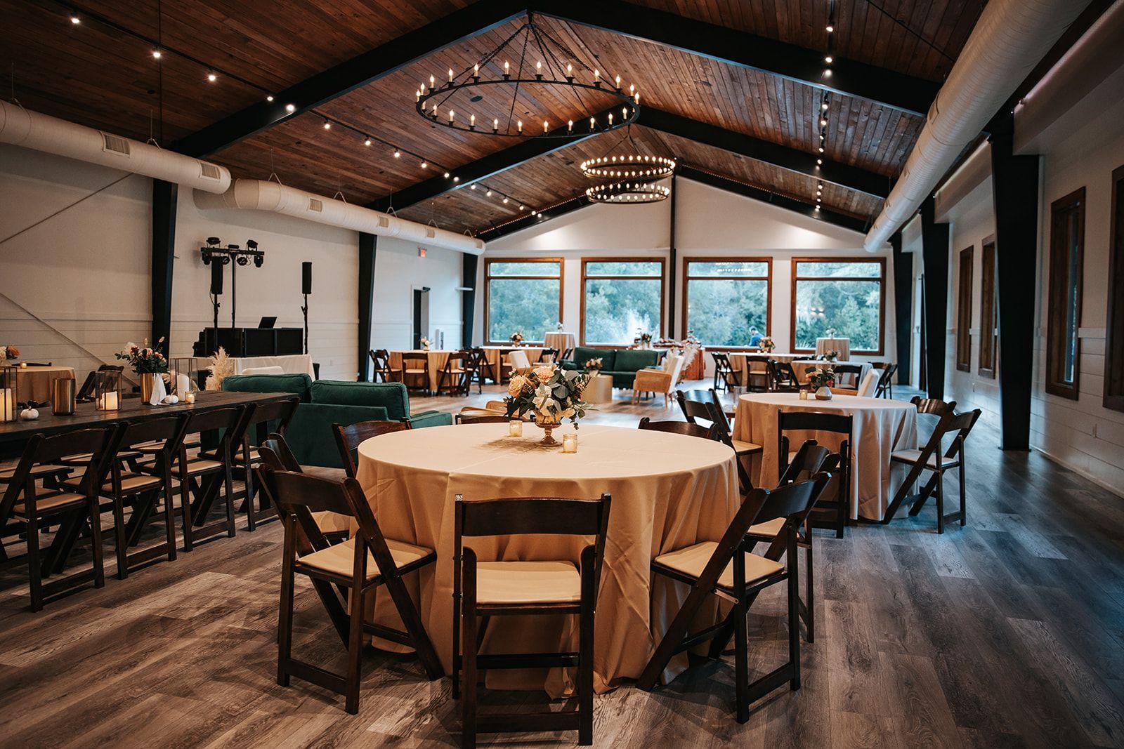 Elegant dining hall with round tables, wooden chairs, and warm string lights under a high vaulted ceiling