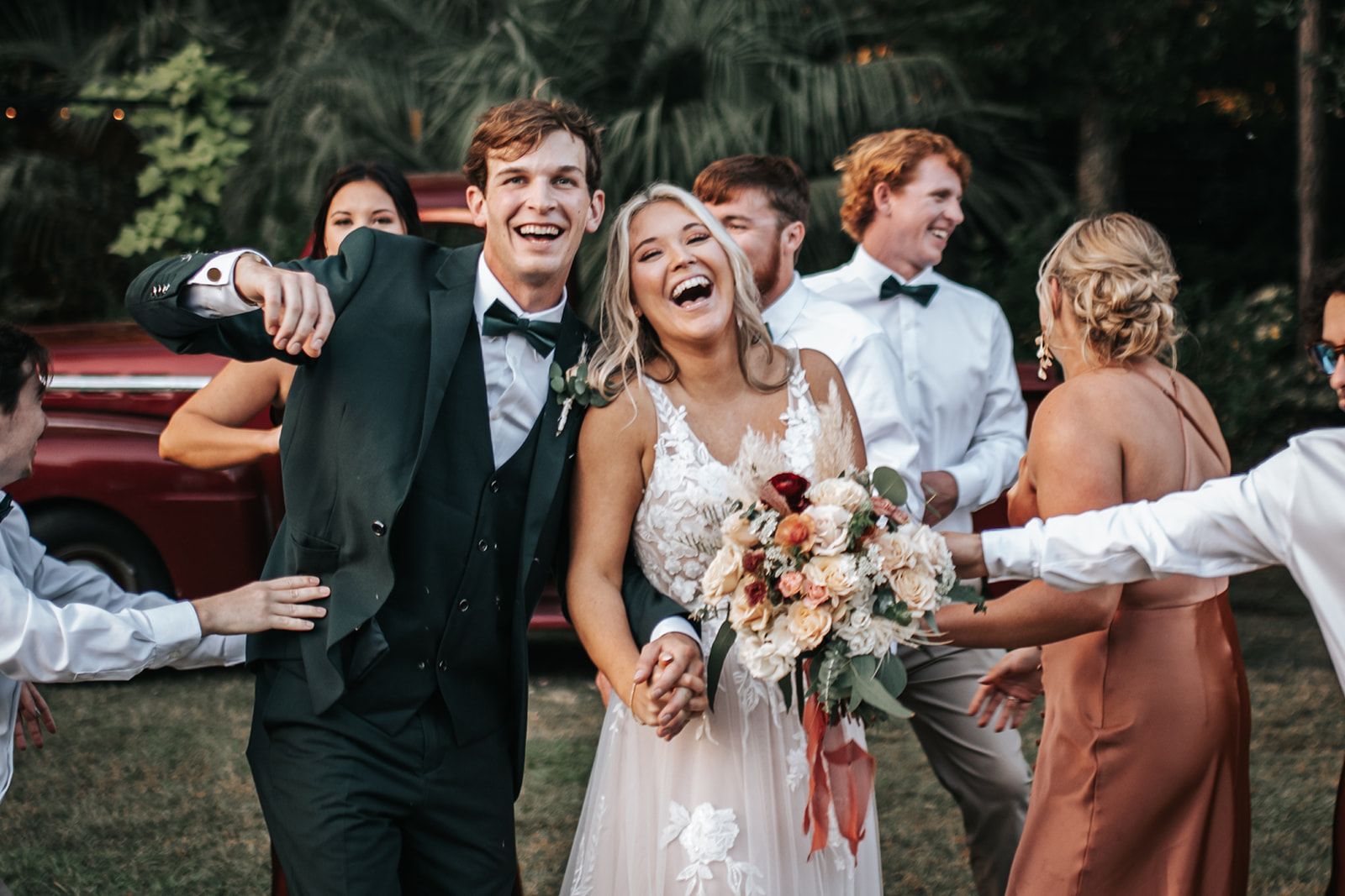 Wedding party celebrating outdoors, smiling and dancing with the bride holding a bouquet.