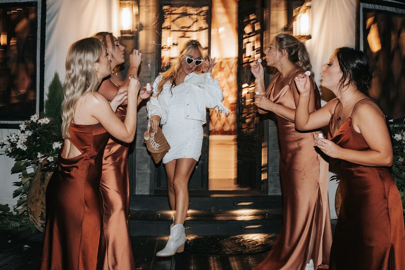 Group of people celebrating in formal dresses, laughing and clinking drinks at a party entrance.