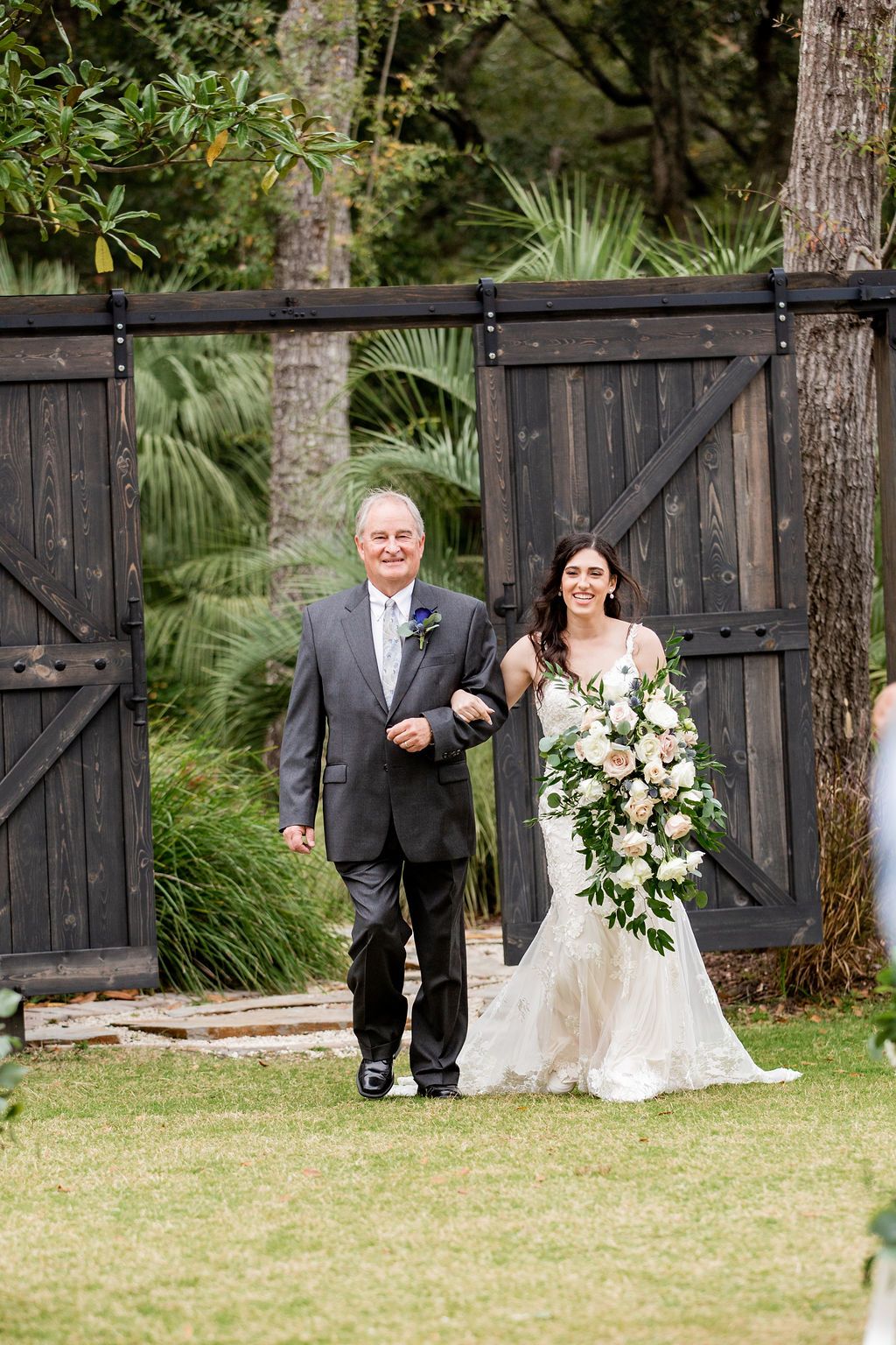 Bride and older man walking arm-in-arm through a wooden gate in a garden wedding setting