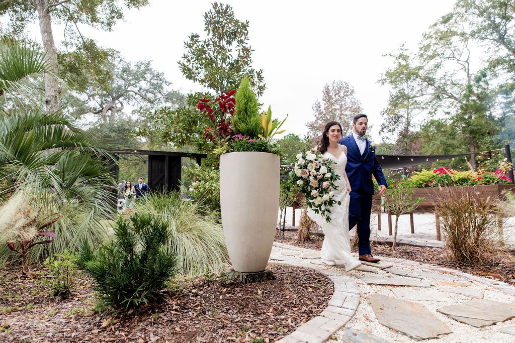 Bride and groom walking along a garden path, surrounded by lush greenery and flowers.