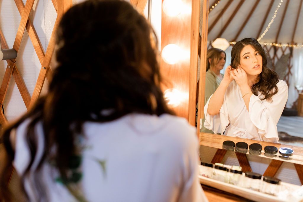 Woman applying lipstick while looking in a vanity mirror in a warmly lit room