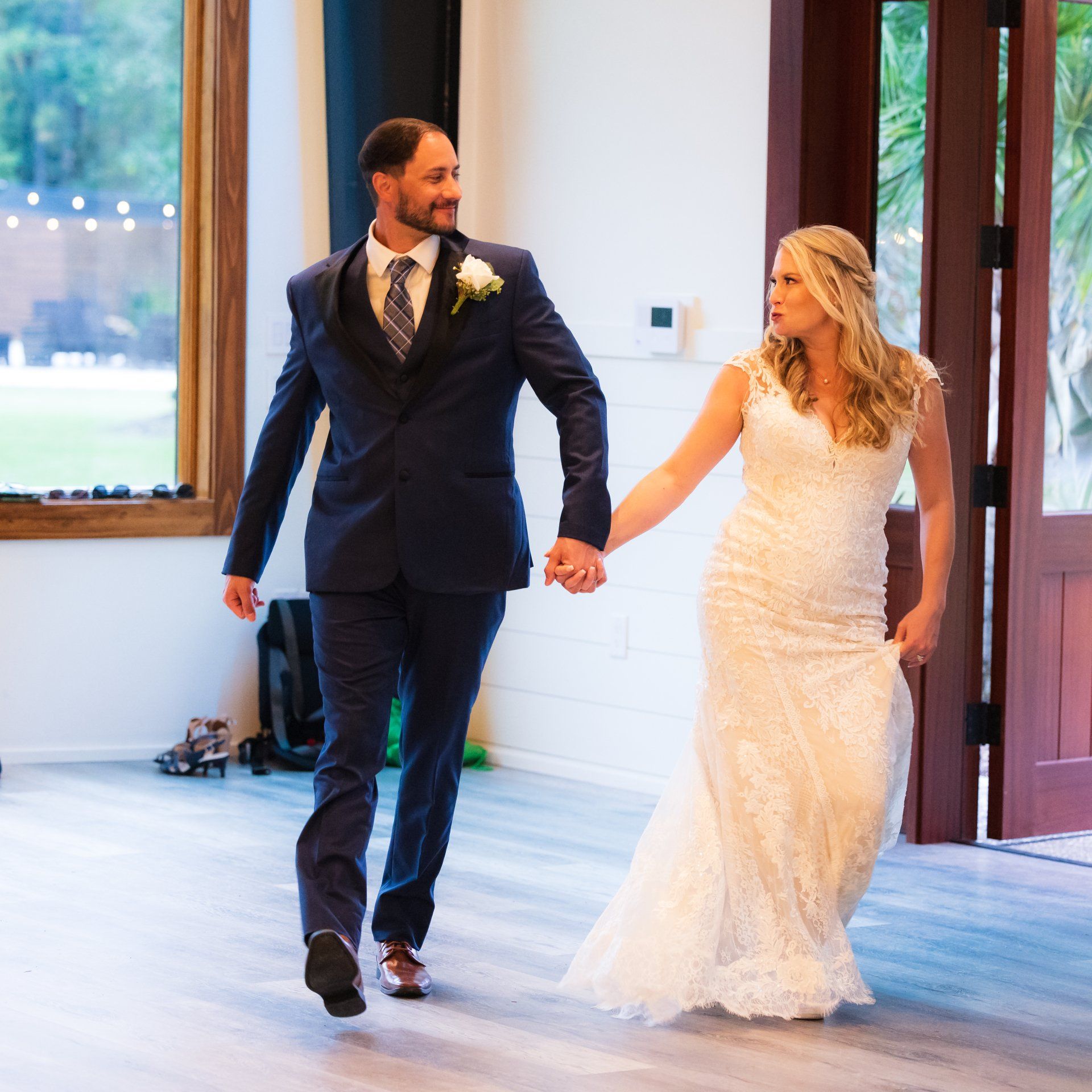 Bride and groom holding hands and walking into a bright venue, smiling