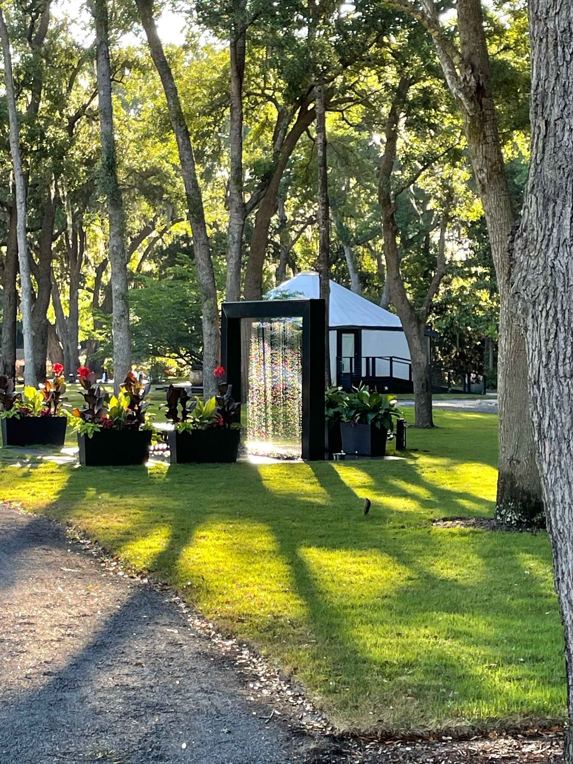 Garden path beside a black-and-white pavilion among tall trees in dappled sunlight