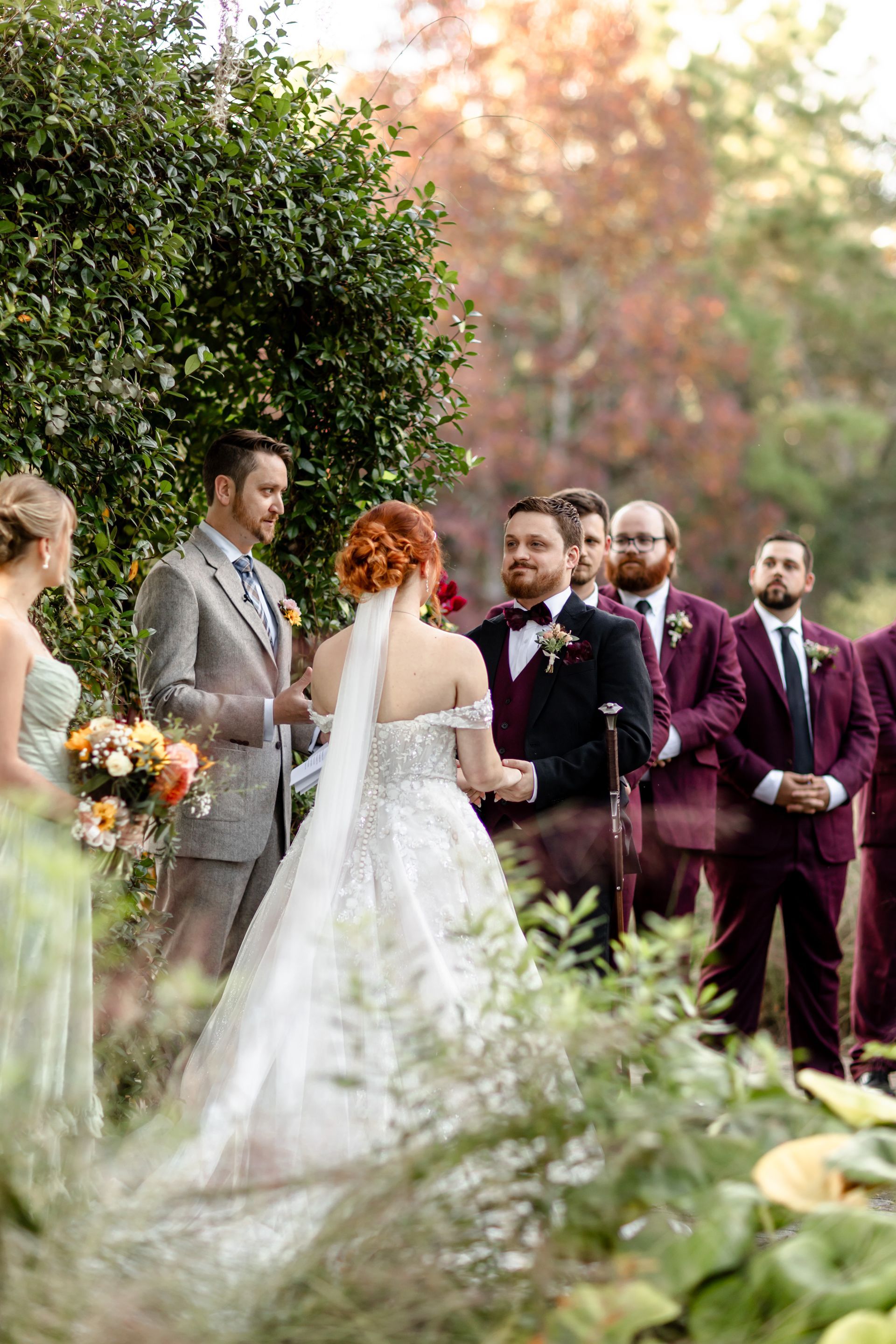 Wedding couple exchanging vows outdoors with attendants standing nearby in a garden setting