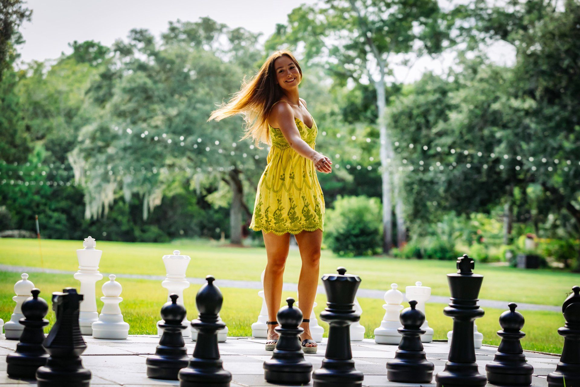 Woman in a yellow dress standing on oversized chess pieces in a park