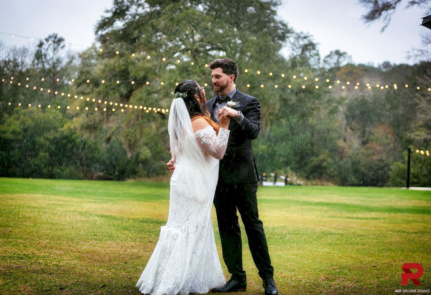 Bride and groom dancing outdoors under string lights in a grassy park