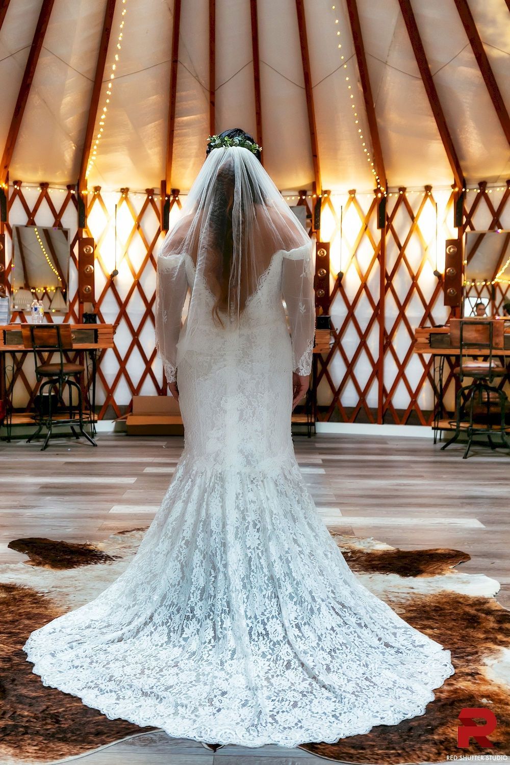 Bride in a white lace gown with a long train and veil standing inside a tepee wedding venue