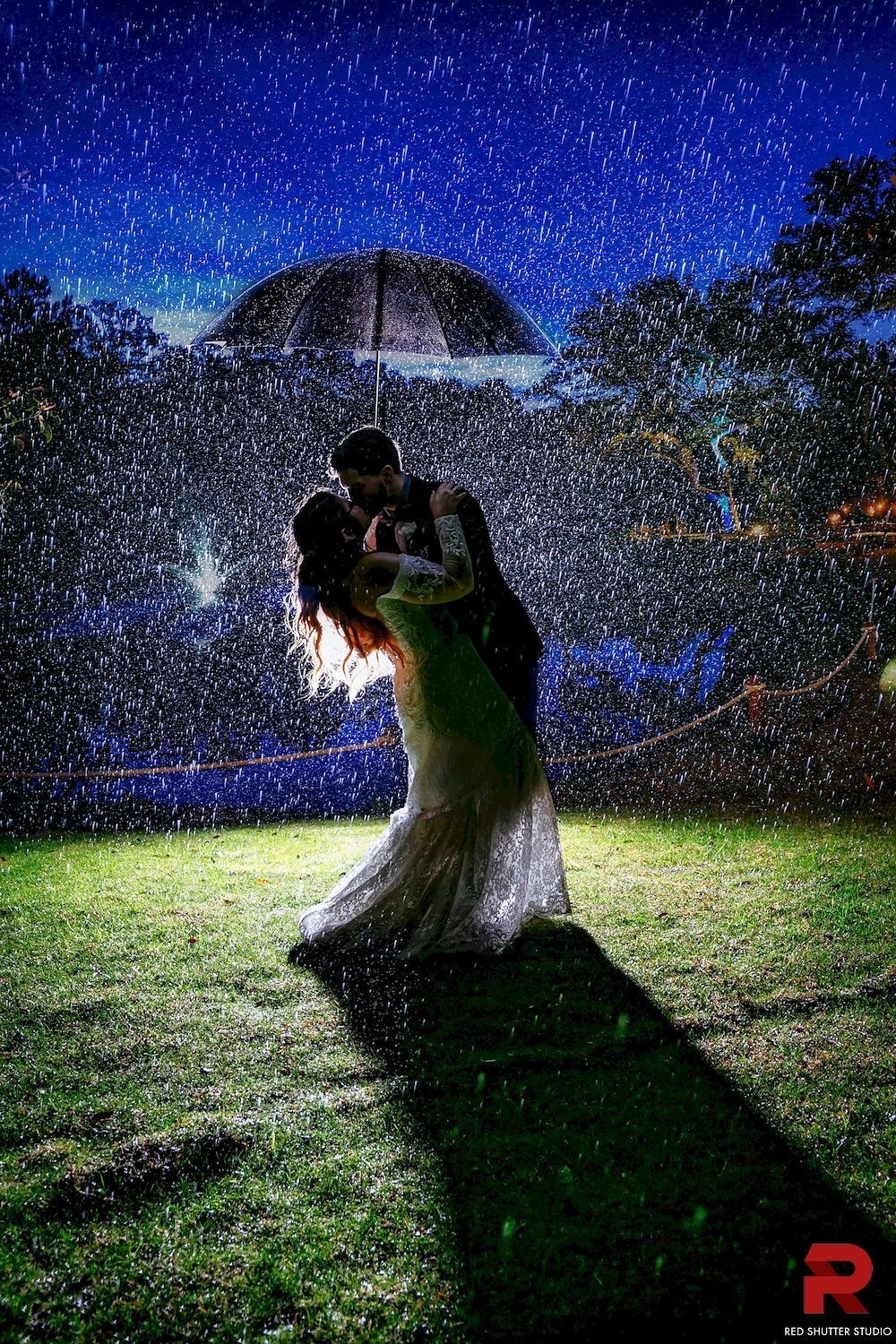 Couple embracing in the rain under an umbrella, lit by city lights at night.