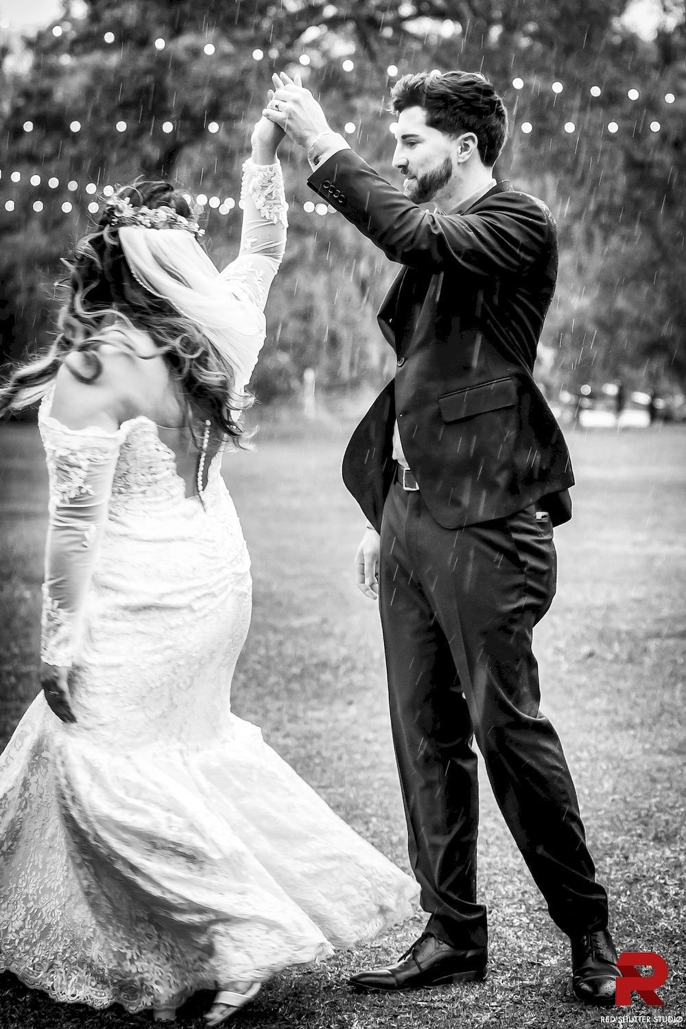Bride and groom dance outdoors under string lights, holding hands in a joyful wedding moment.