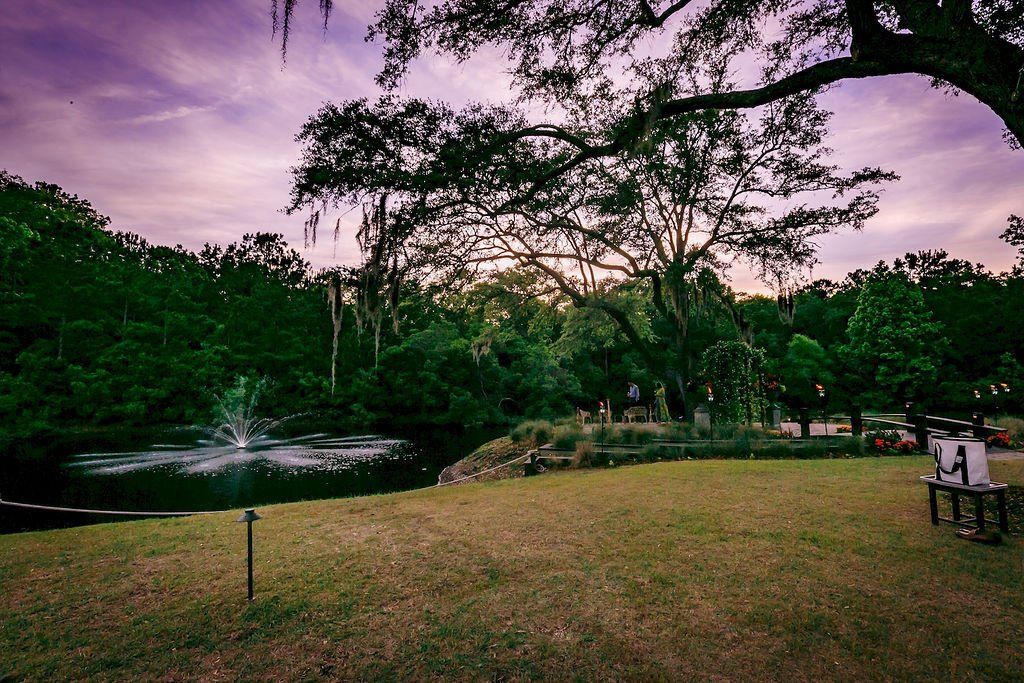 Park lawn by a small pond at dusk, with trees silhouetted against a purple sky.