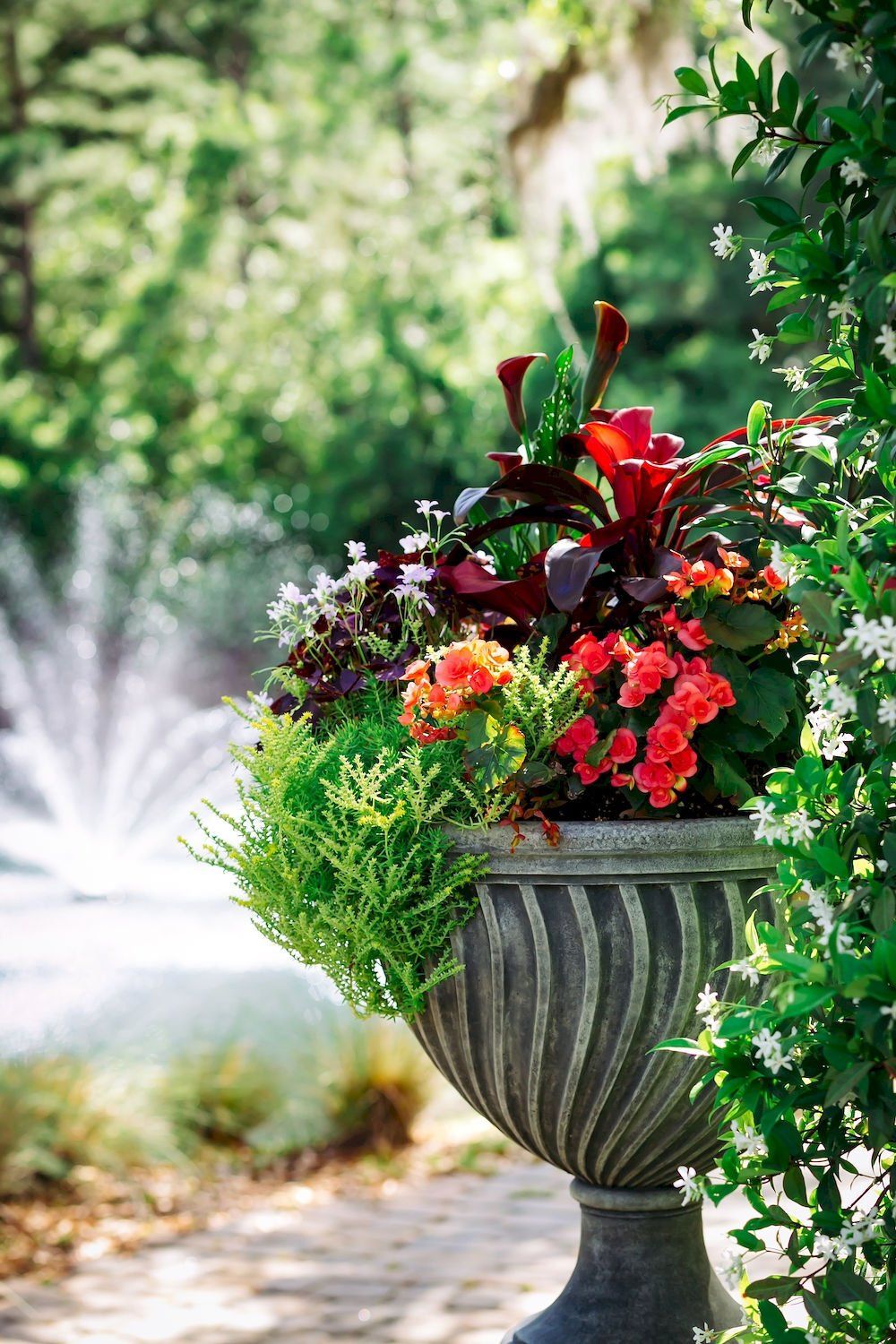 Ornate stone urn overflowing with red and green flowers in a sunny garden