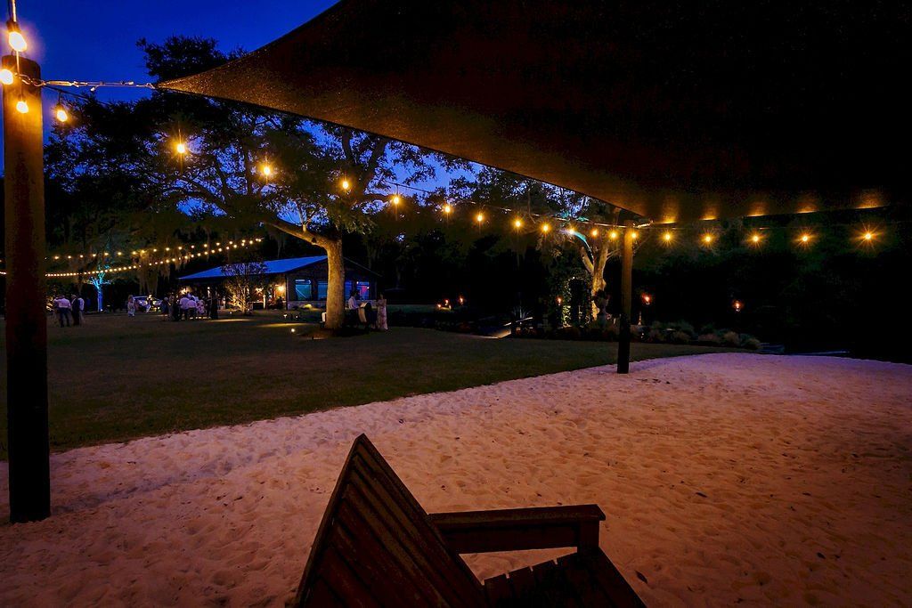 Lit outdoor patio with string lights, sandy seating area, and trees at night