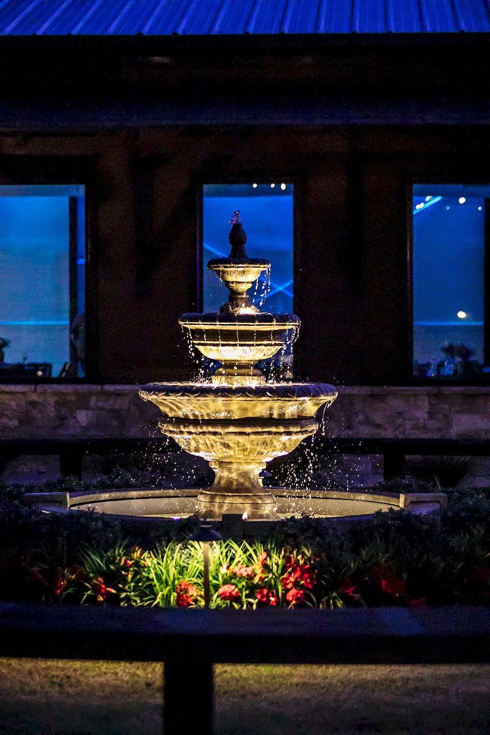 Lit tiered fountain glowing at night outside a building with blue-lit windows.