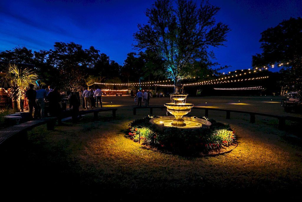 Illuminated garden fountain at night with string lights and a deep blue sky