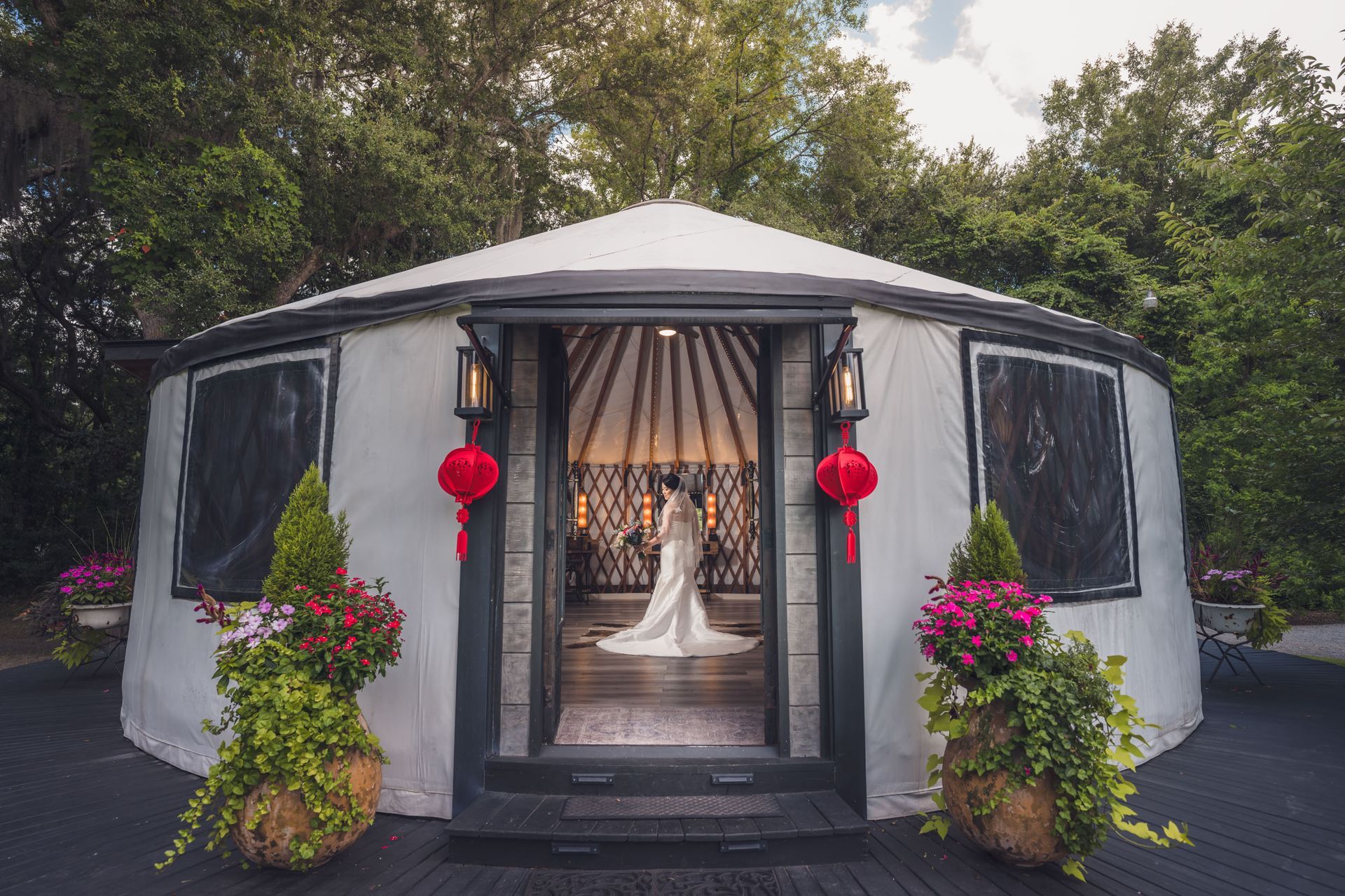 White wedding tent with black trim, red lanterns, flower pots, and a draped aisle leading inside