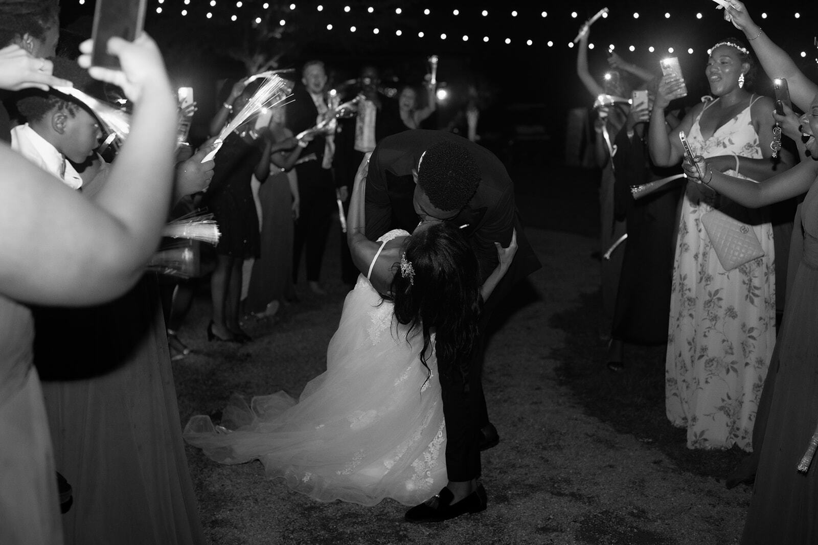 Bride and groom kissing at a nighttime outdoor wedding reception while guests watch nearby