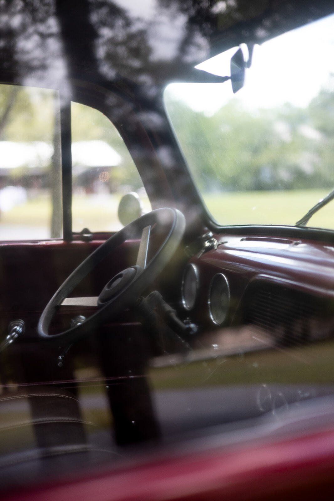Interior of a vintage car with a black steering wheel and red dashboard, viewed through a window.