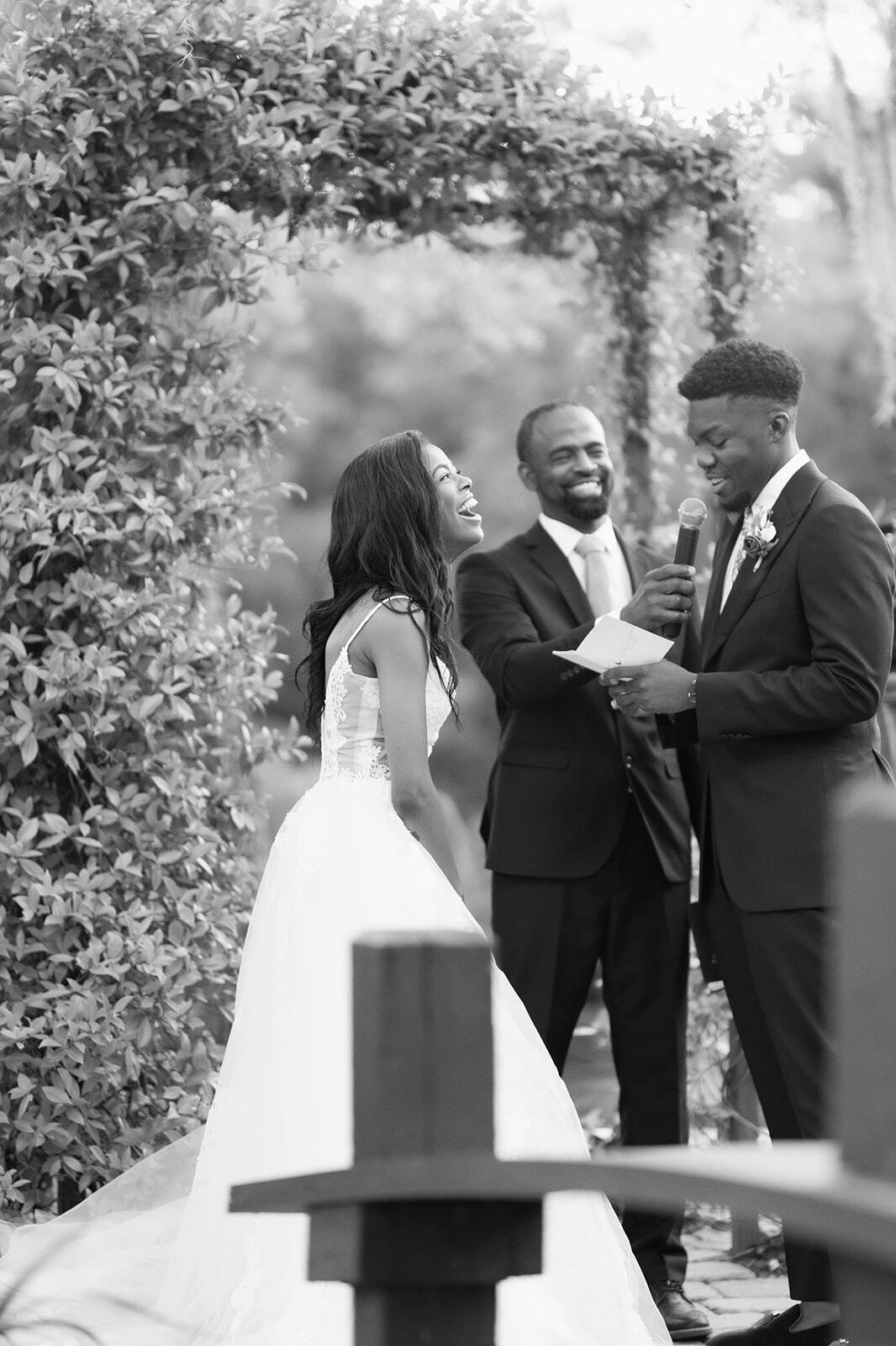 Wedding couple and officiant smiling outdoors near a leafy archway