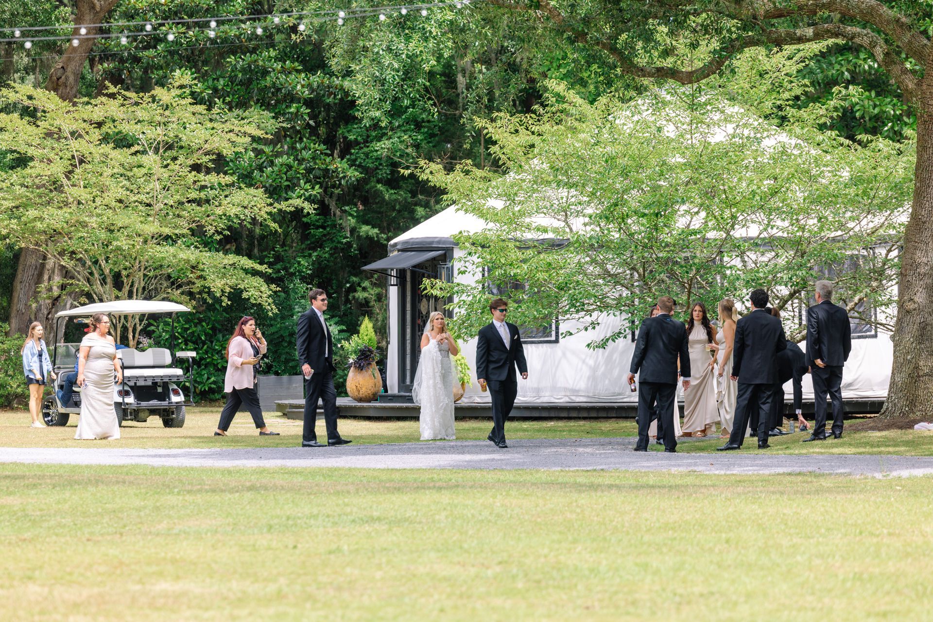 People gathered near a park information sign under leafy trees on a sunny day.