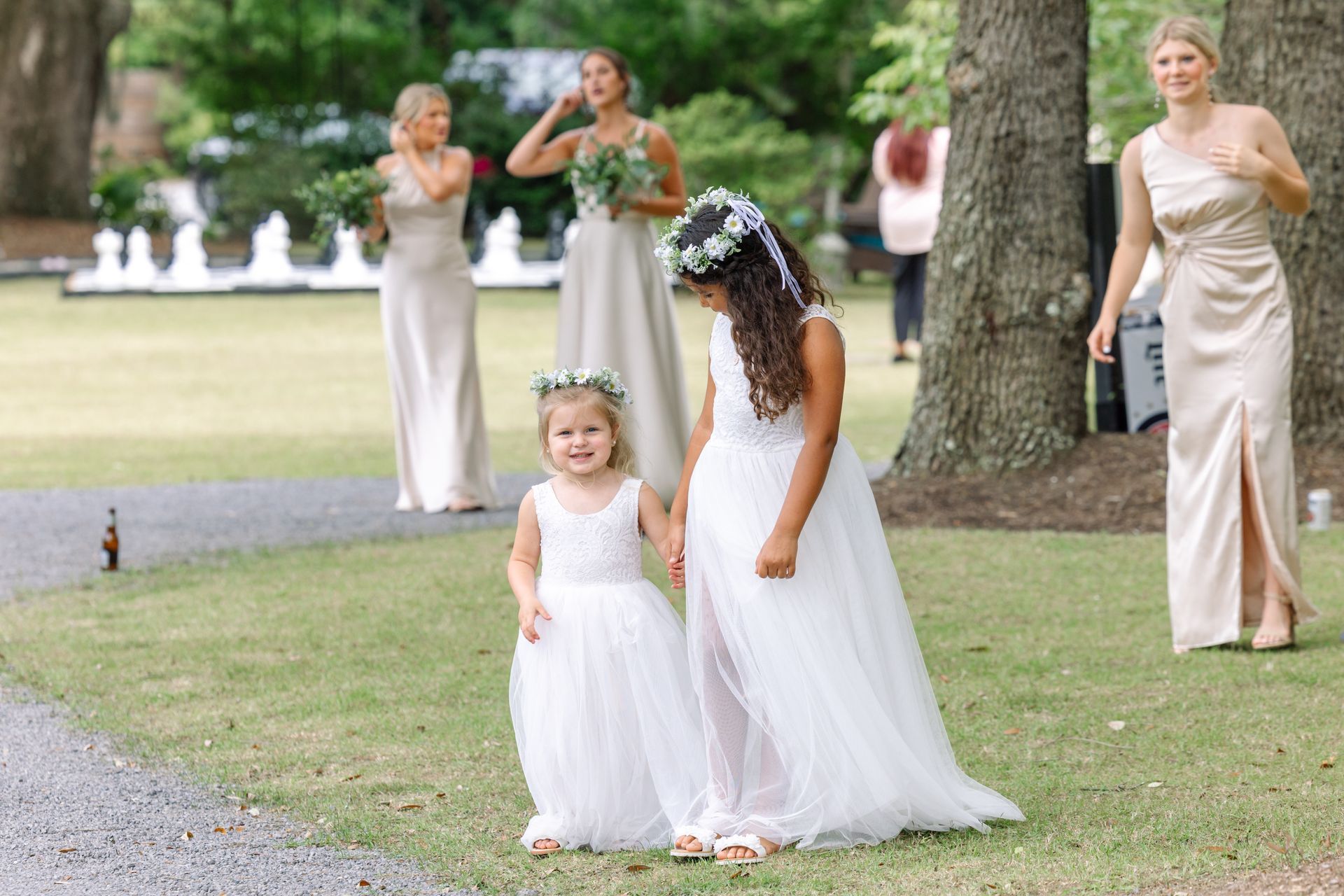 Bride with flower girl in white dresses at an outdoor wedding, bridesmaids standing behind them