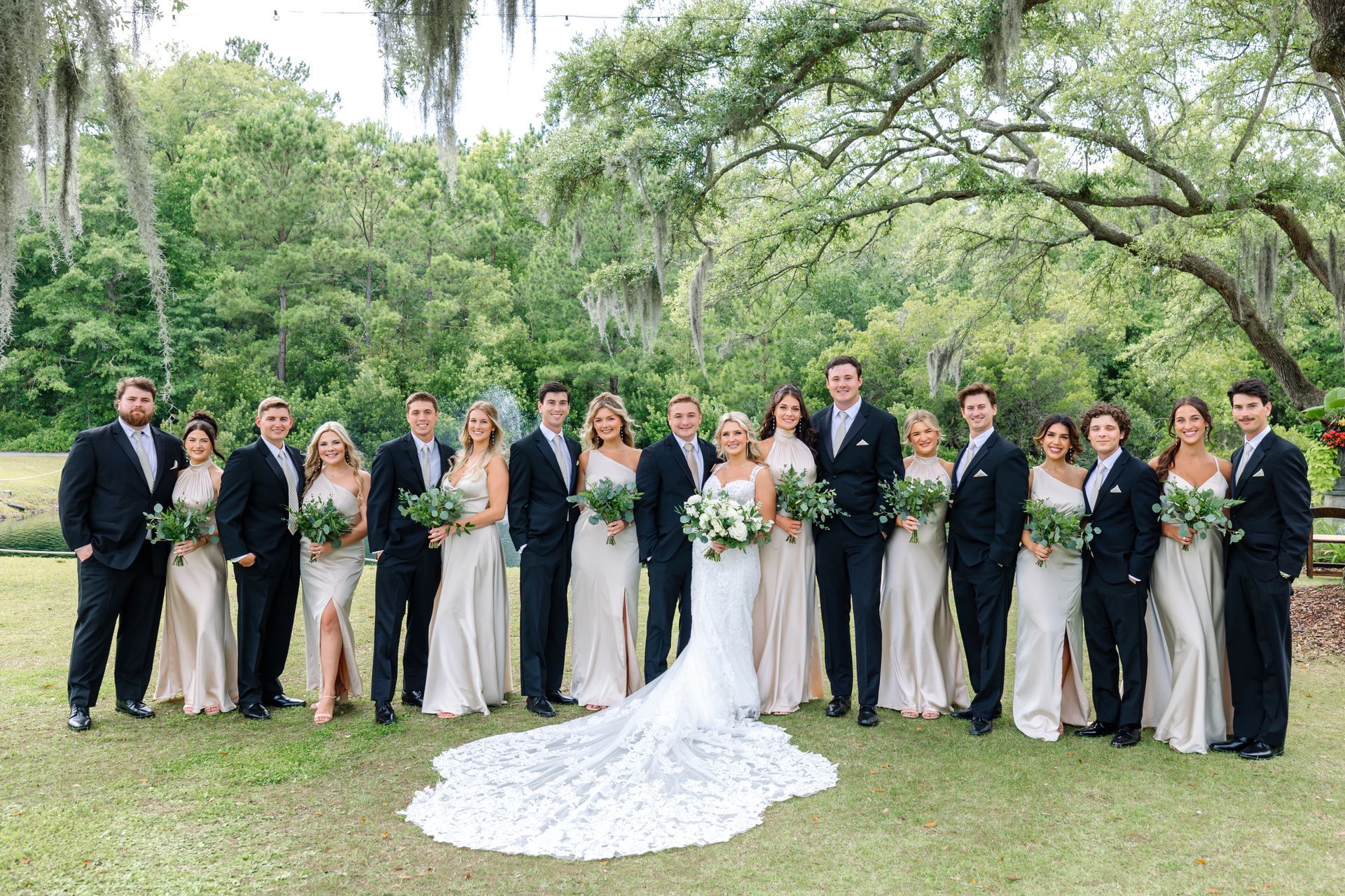 Wedding party posing outdoors in formal black-and-white attire with the bride in a long white gown and bouquet