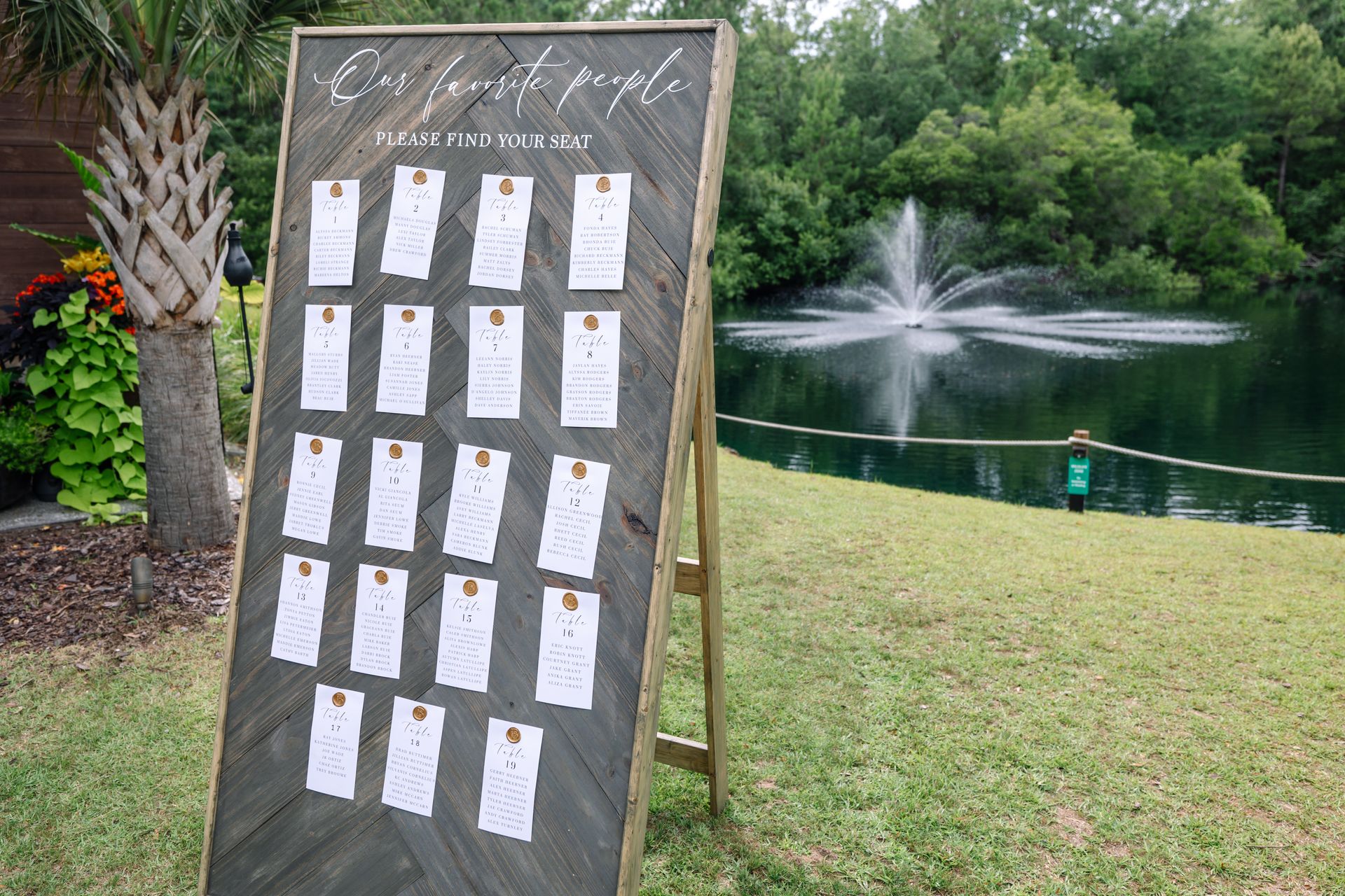 Outdoor display board beside a pond fountain, with rows of paper cards and lush greenery in the background