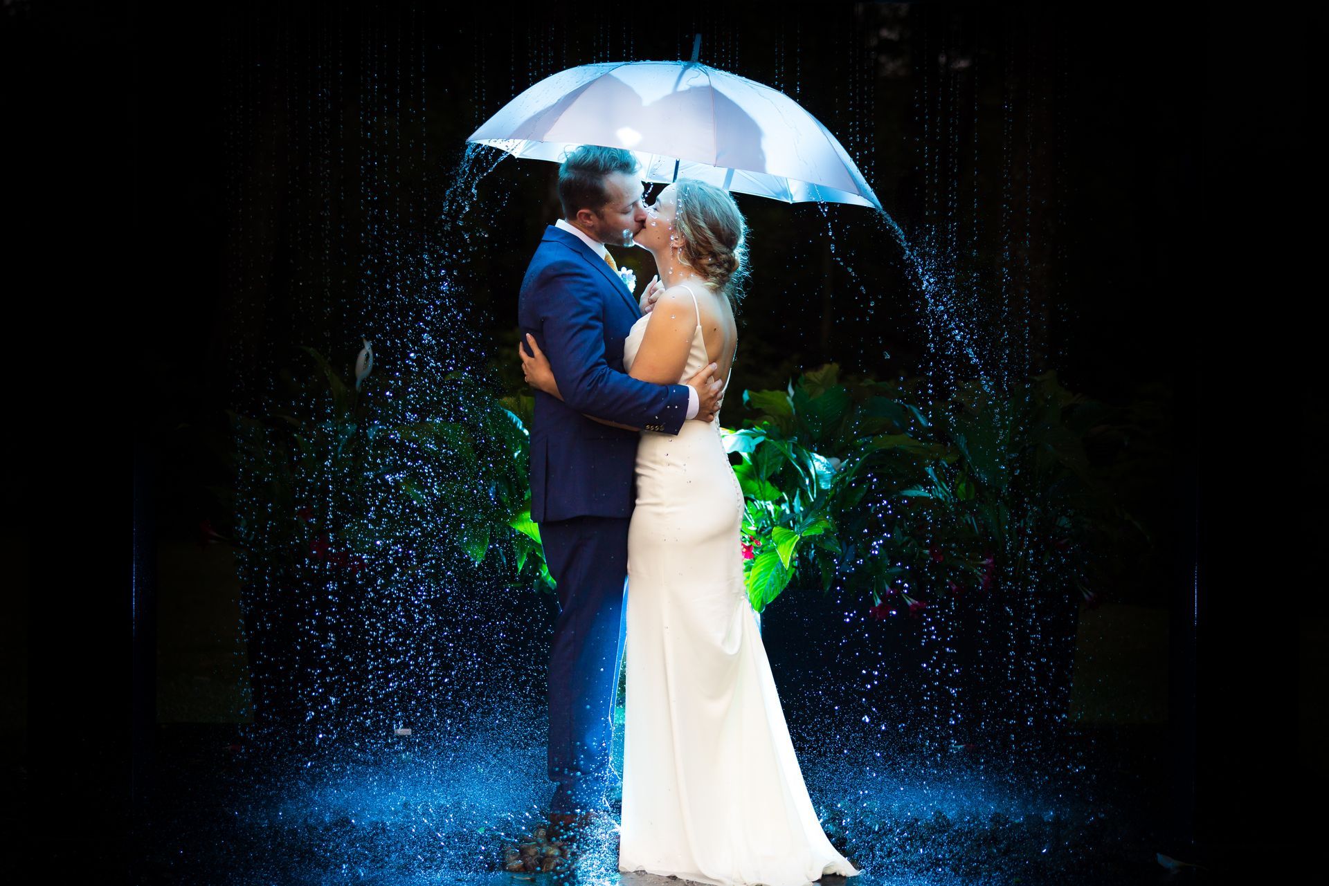 Couple embracing under a glowing umbrella, surrounded by blue light and sparkling particles on a dark stage