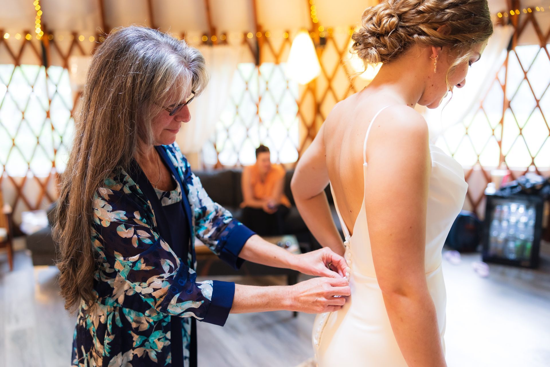 Designer adjusts a cream gown on a model in a bright dressing room
