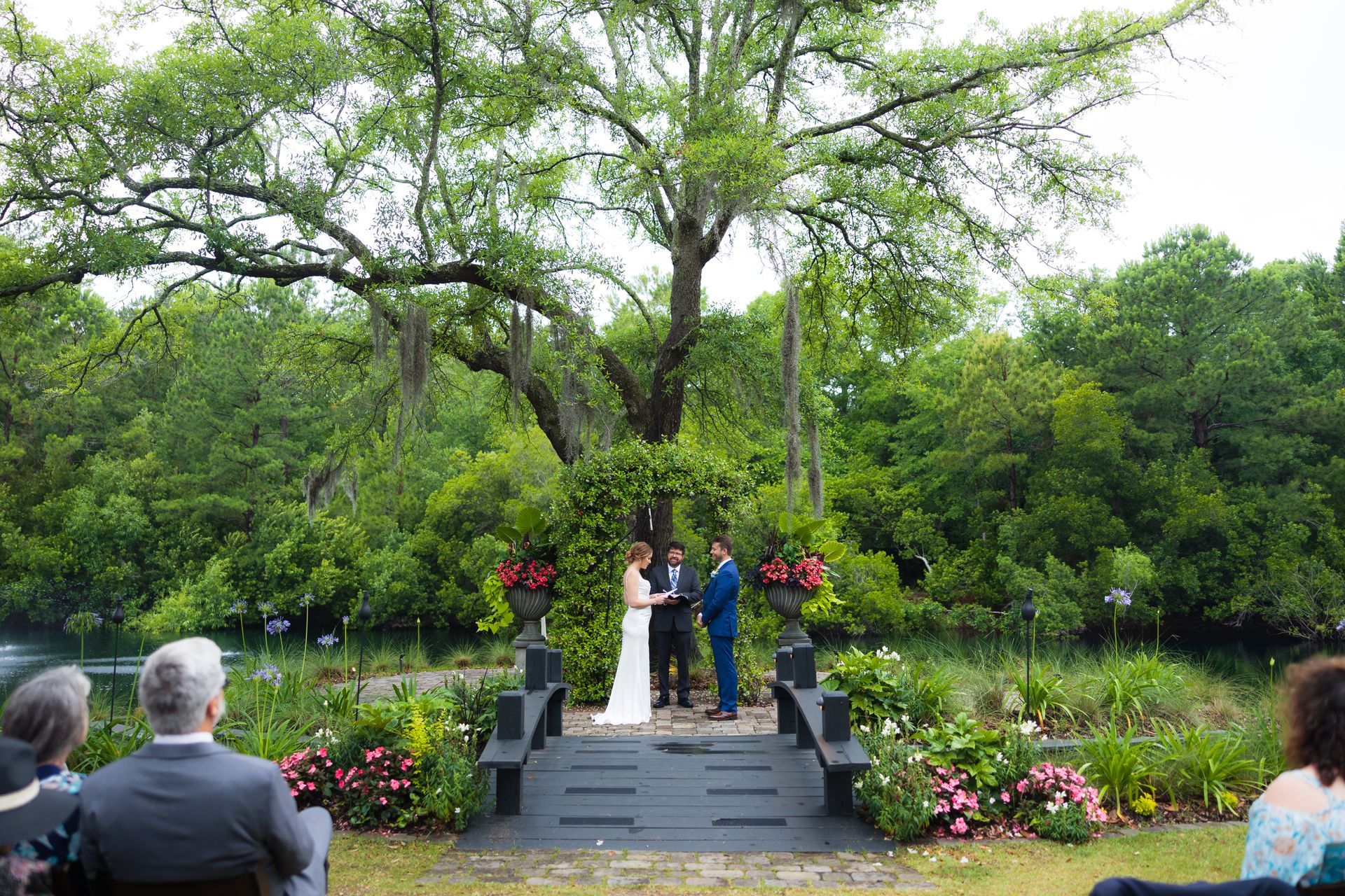 People standing on a small stage in a lush garden, with seated audience members in the foreground.