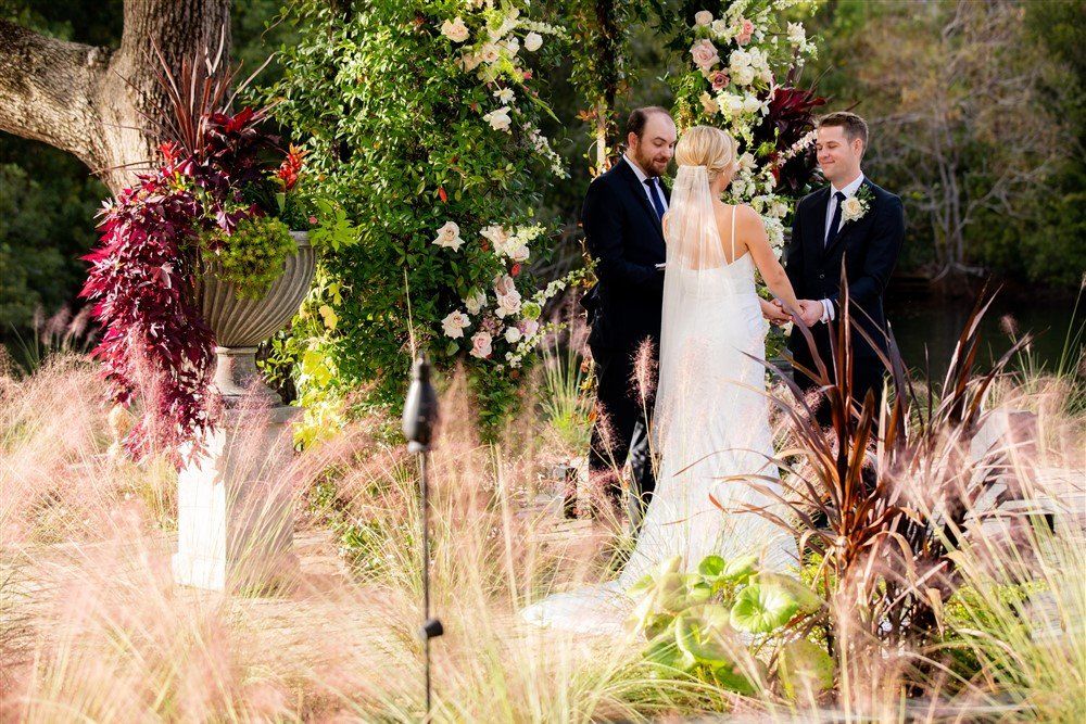 Wedding couple and officiant standing among floral arrangements in a garden setting