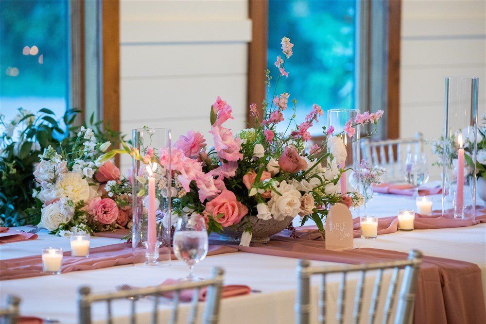 Elegant banquet table with pink and white floral centerpieces, candles, and glassware in a bright dining room
